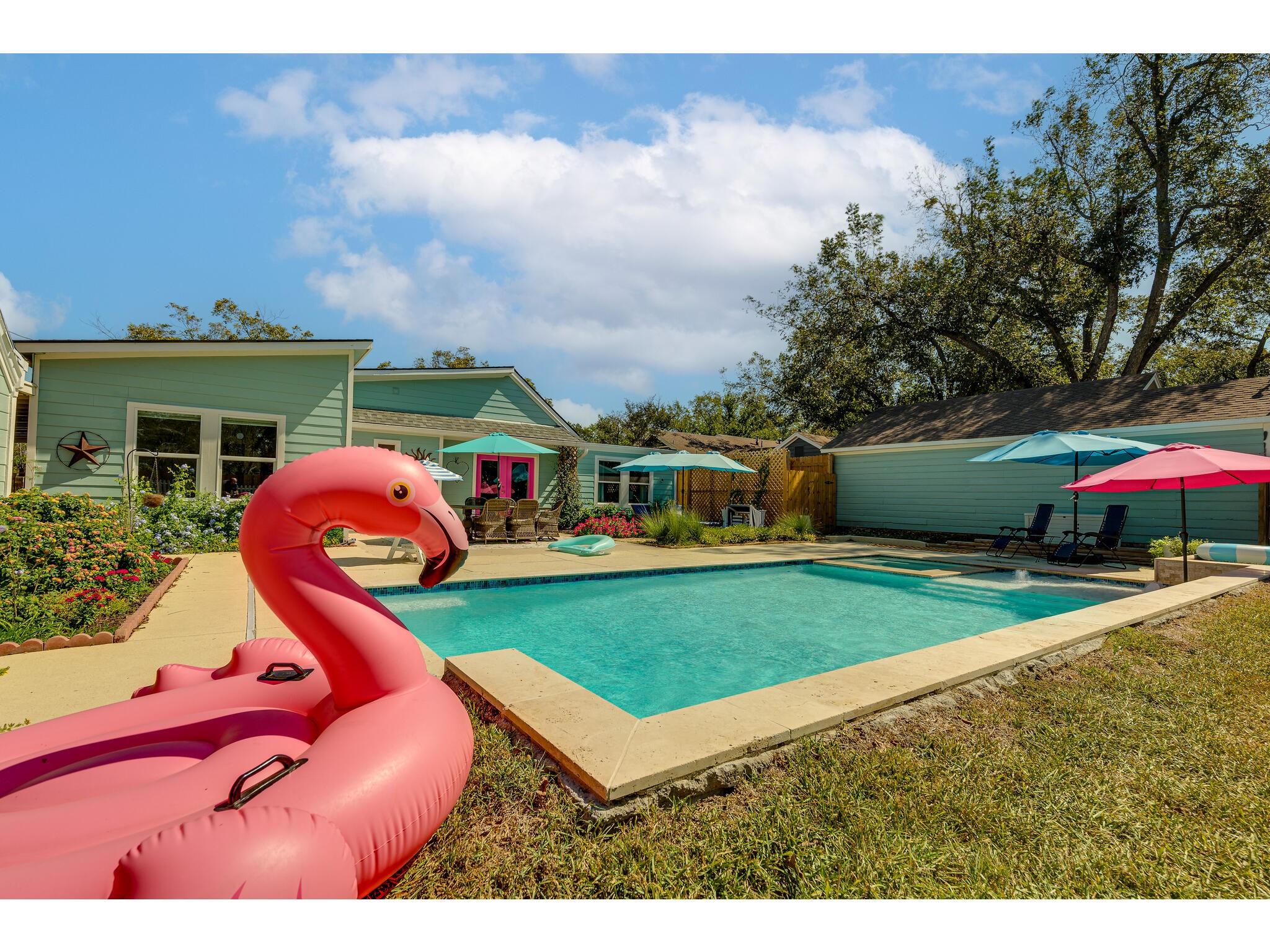 Backyard swimming pool with colorful umbrellas and a large pink flamingo float.