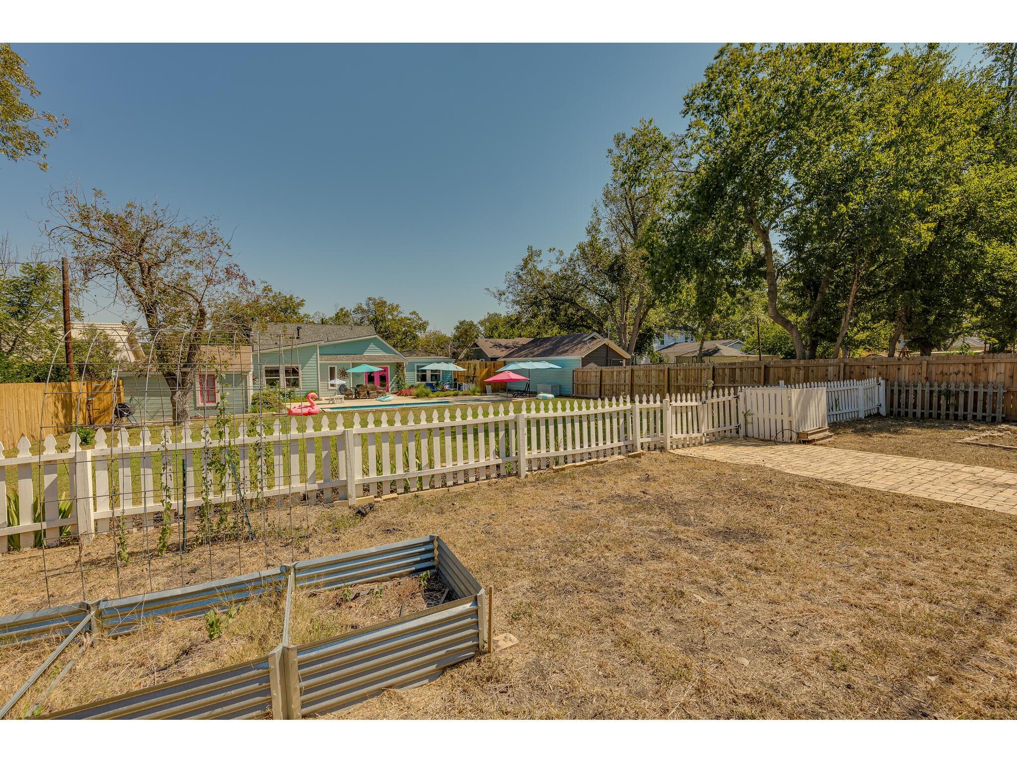 Backyard with raised garden beds, a picket fence, and a view toward the house and pool.