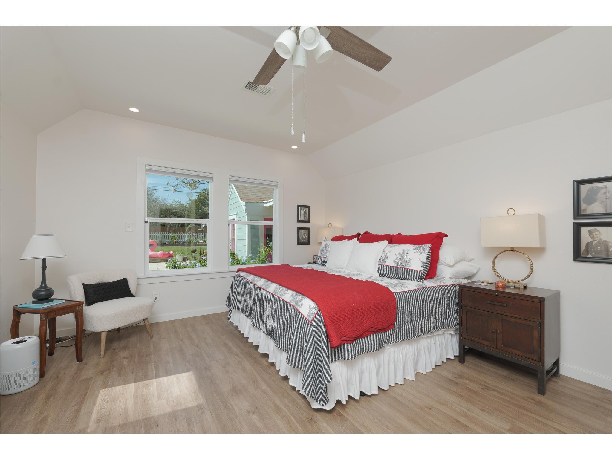 Bedroom with a vaulted ceiling, large bed with red bedding, and windows overlooking a garden.
