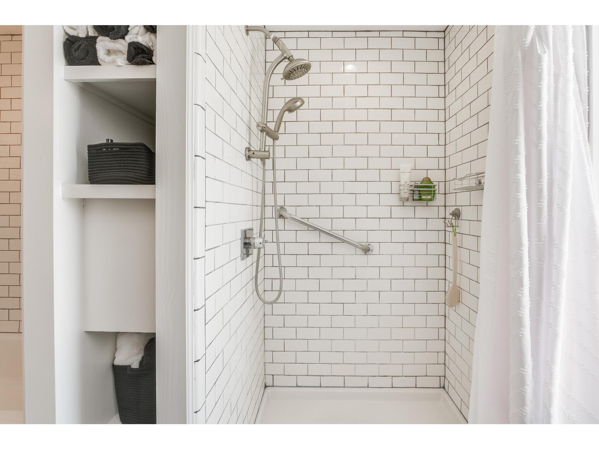 Walk-in shower with white subway tile, dual showerheads, a grab bar, and recessed towel shelves.
