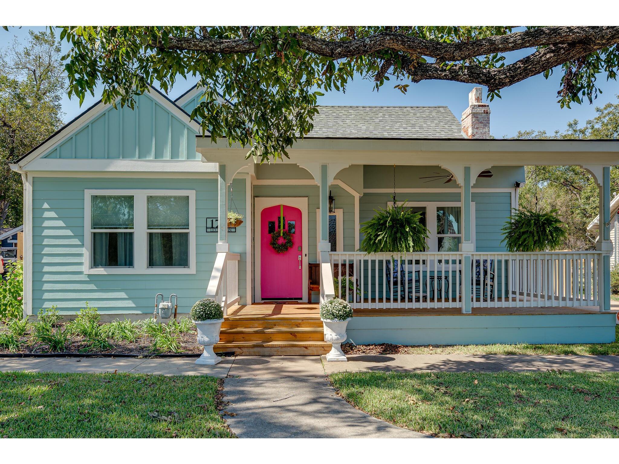 Pale blue house with a covered porch and vivid pink front door.