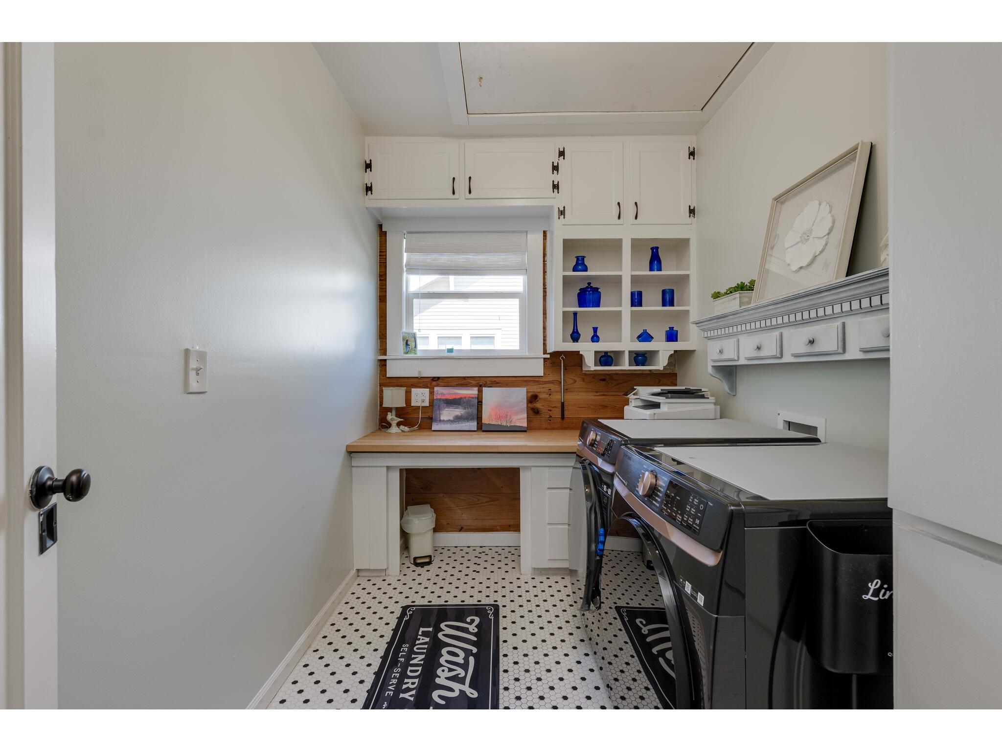 Laundry room with dark washer and dryer, white cabinetry, blue glass decor, and patterned tile floor.