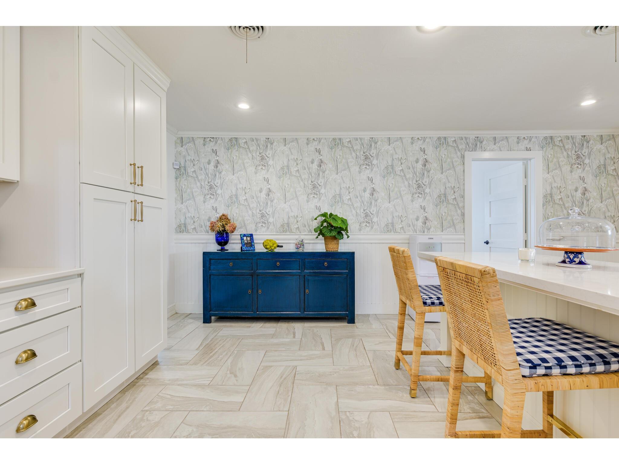 Kitchen dining nook with botanical wallpaper, a deep blue sideboard, and wicker chairs with checked cushions.