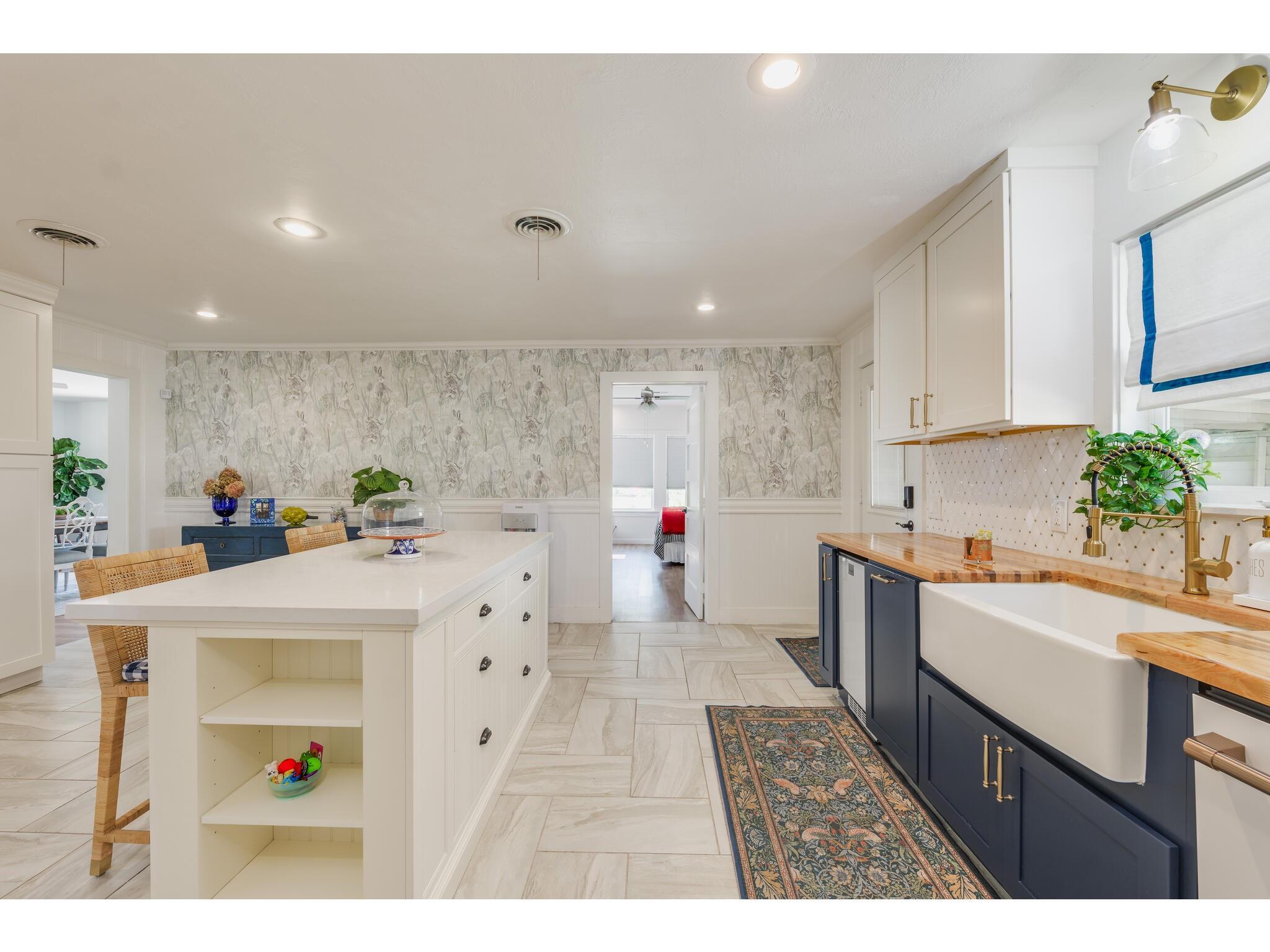 Kitchen with a large white island, navy cabinets, farmhouse sink, and butcher-block countertops.