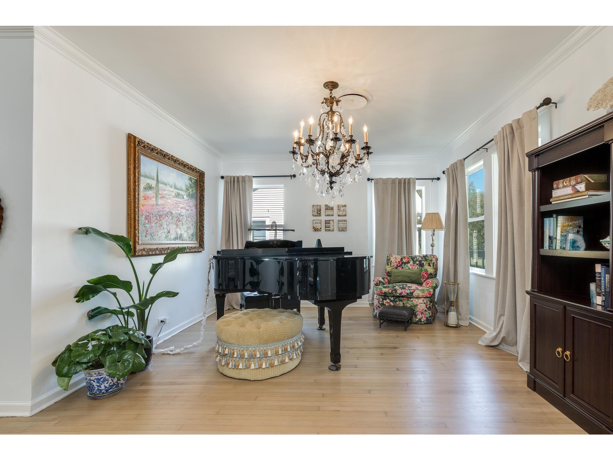 Living room with a black grand piano, crystal chandelier, and floral armchair.
