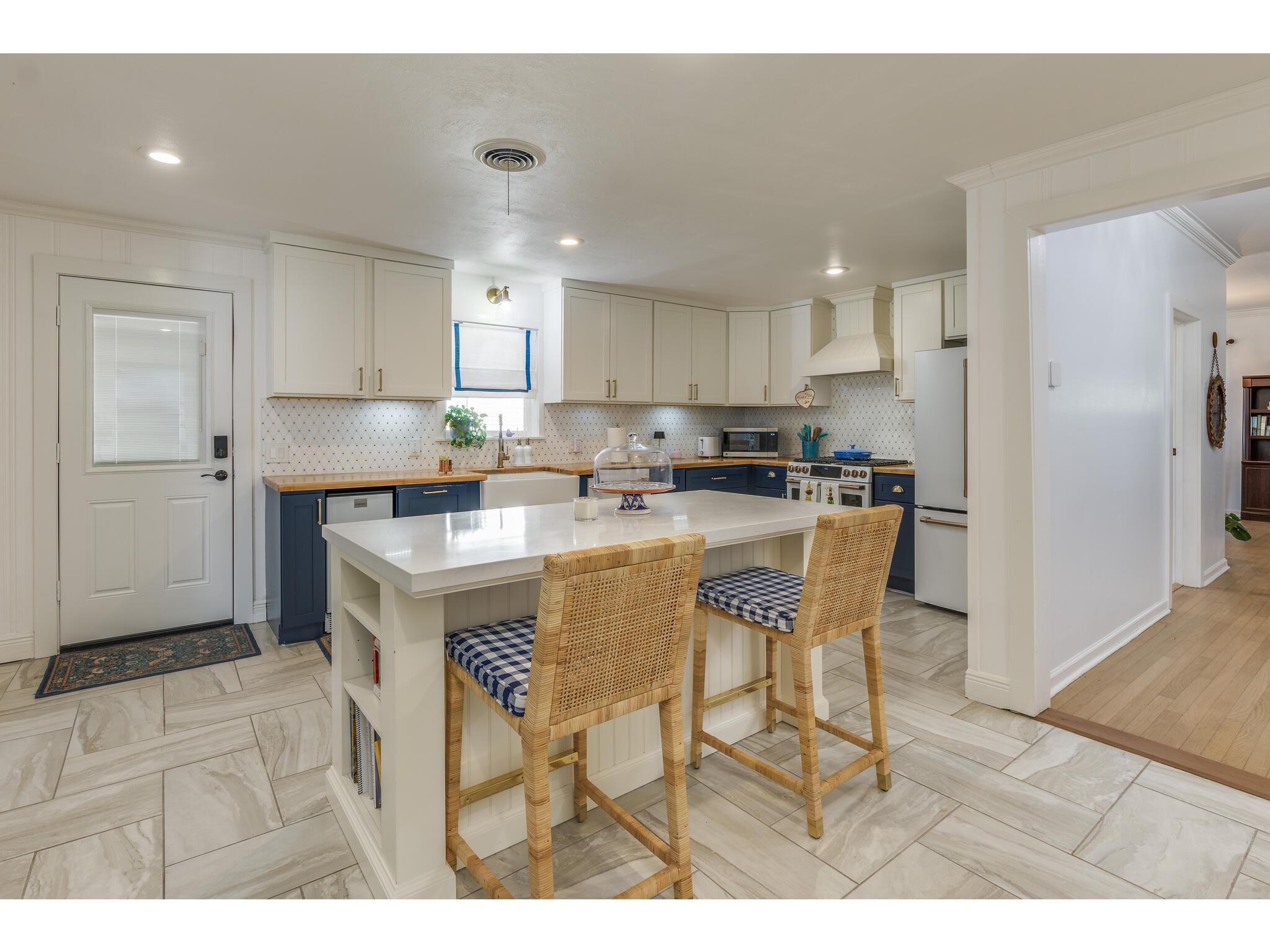 Kitchen with navy lower cabinets, a white island, and wicker bar stools.