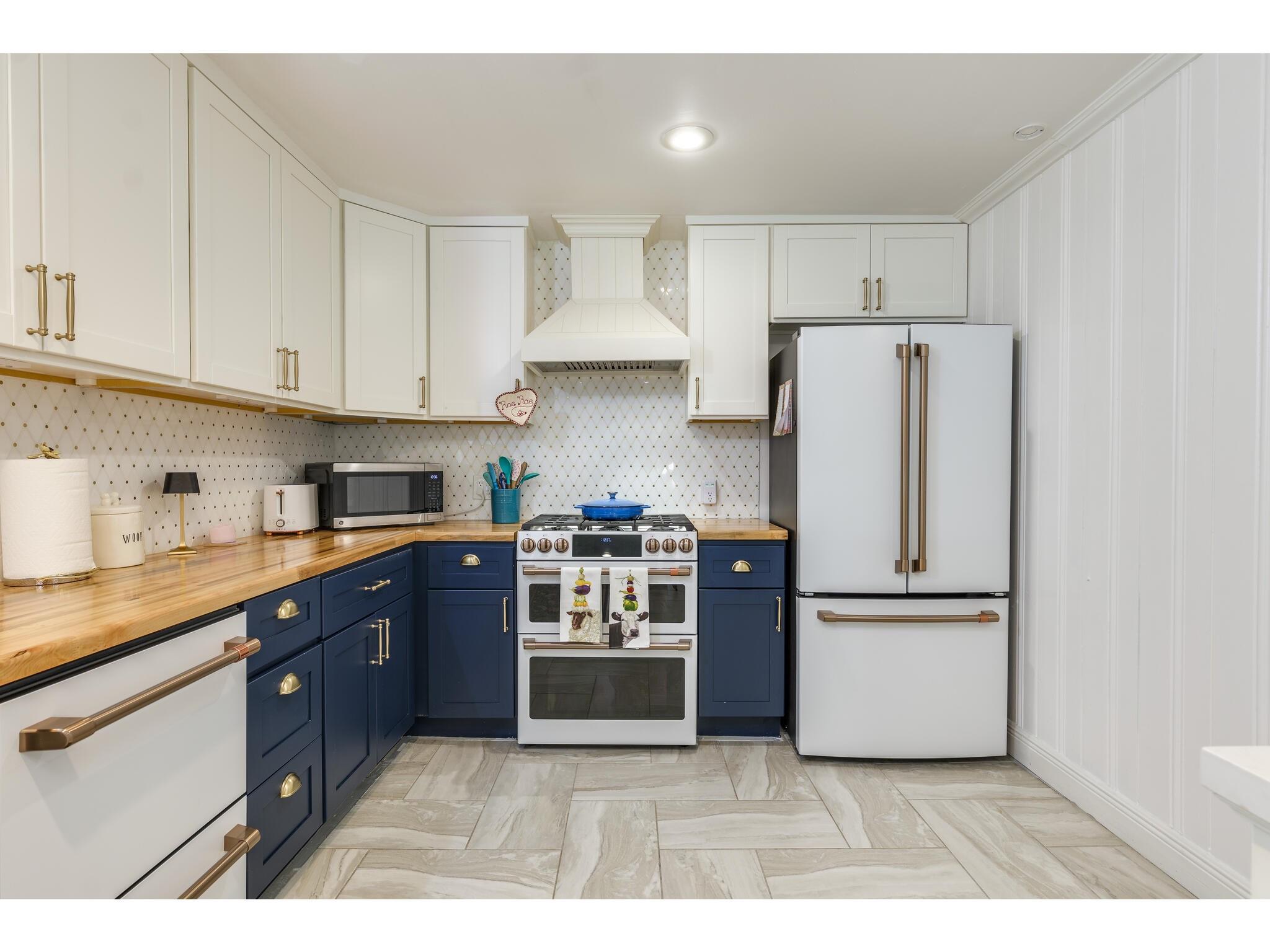 Kitchen with navy lower cabinets, butcher-block counters, and white appliances.