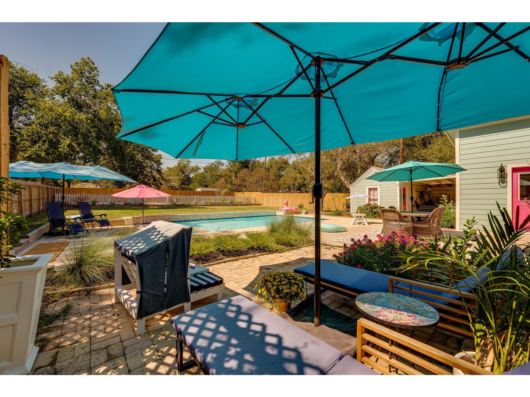 Backyard pool and furnished patio shaded by a large turquoise umbrella.