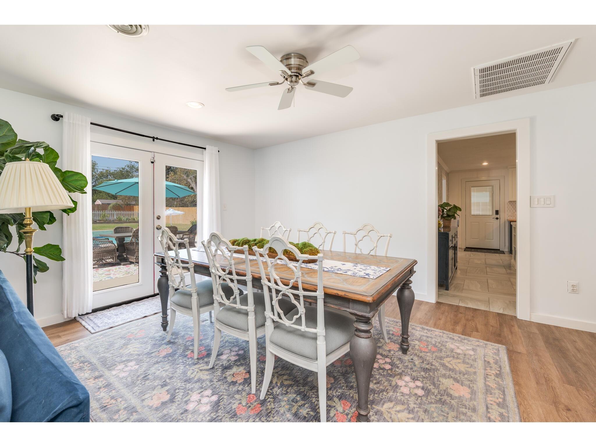 Dining room with a wooden table and white chairs beside French doors overlooking the pool.
