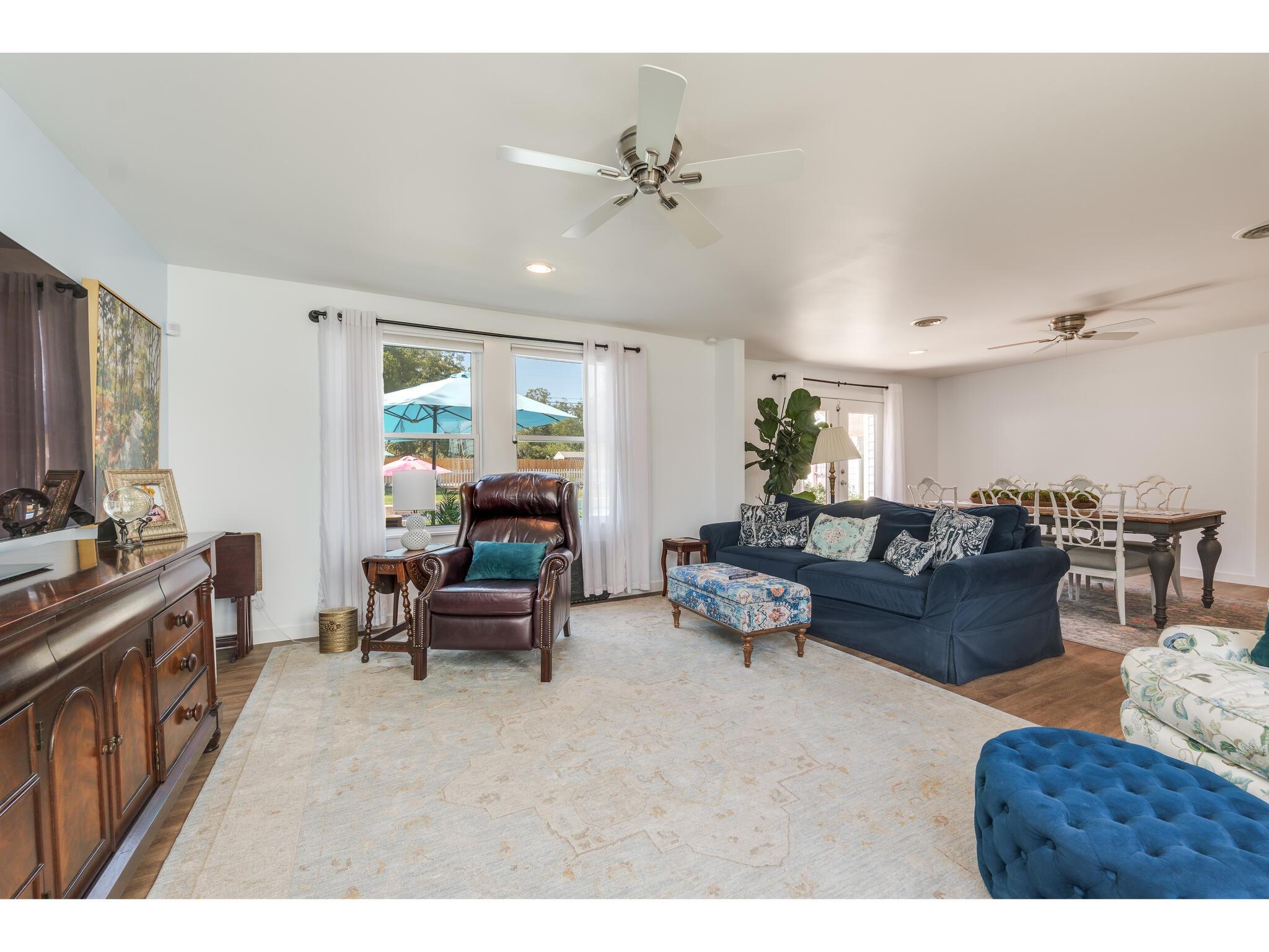 Open-plan living and dining room with a navy sofa, leather armchair, and windows overlooking a patio.