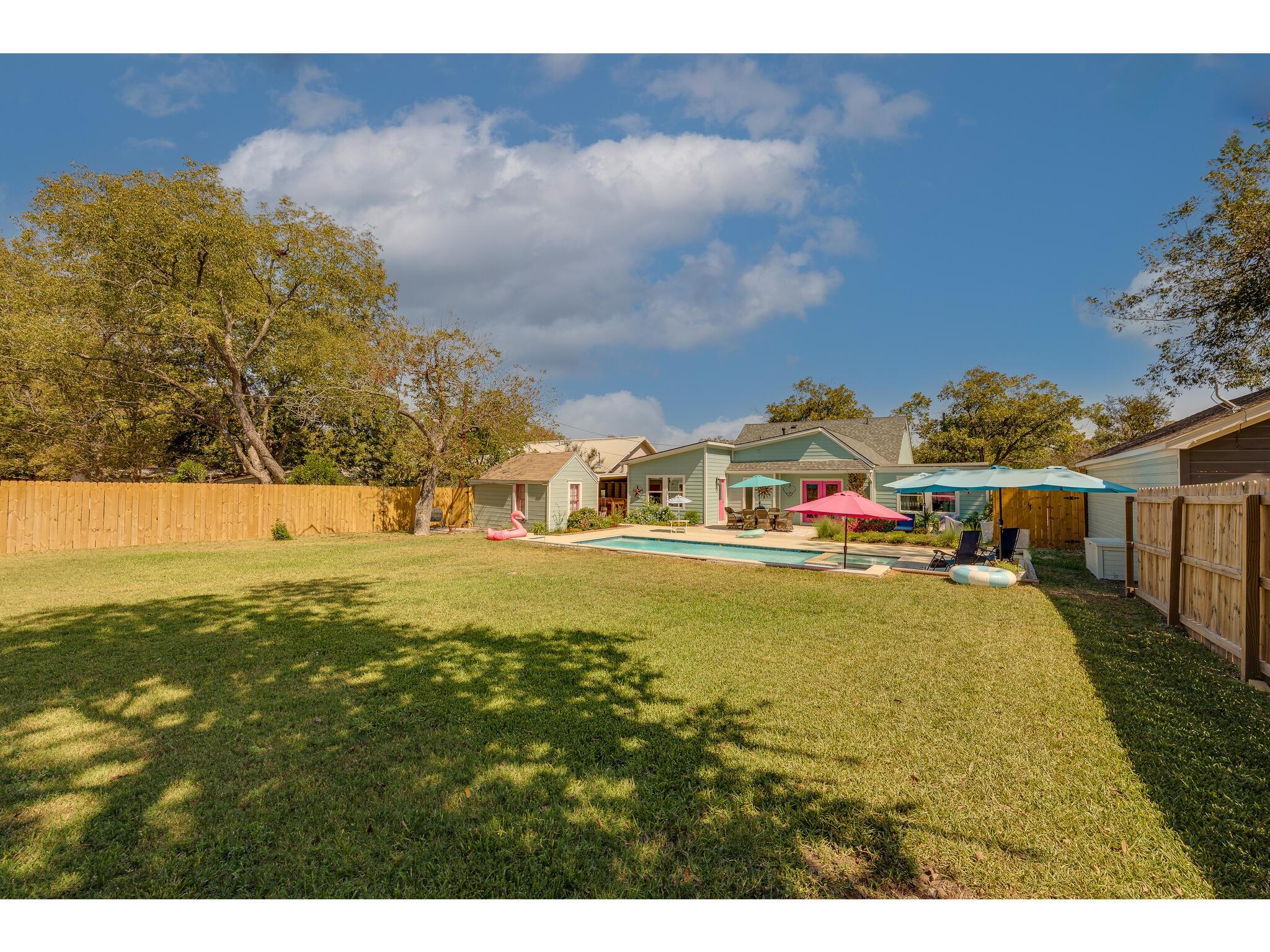 Backyard with a swimming pool, colorful patio umbrellas, and lawn behind a green house.