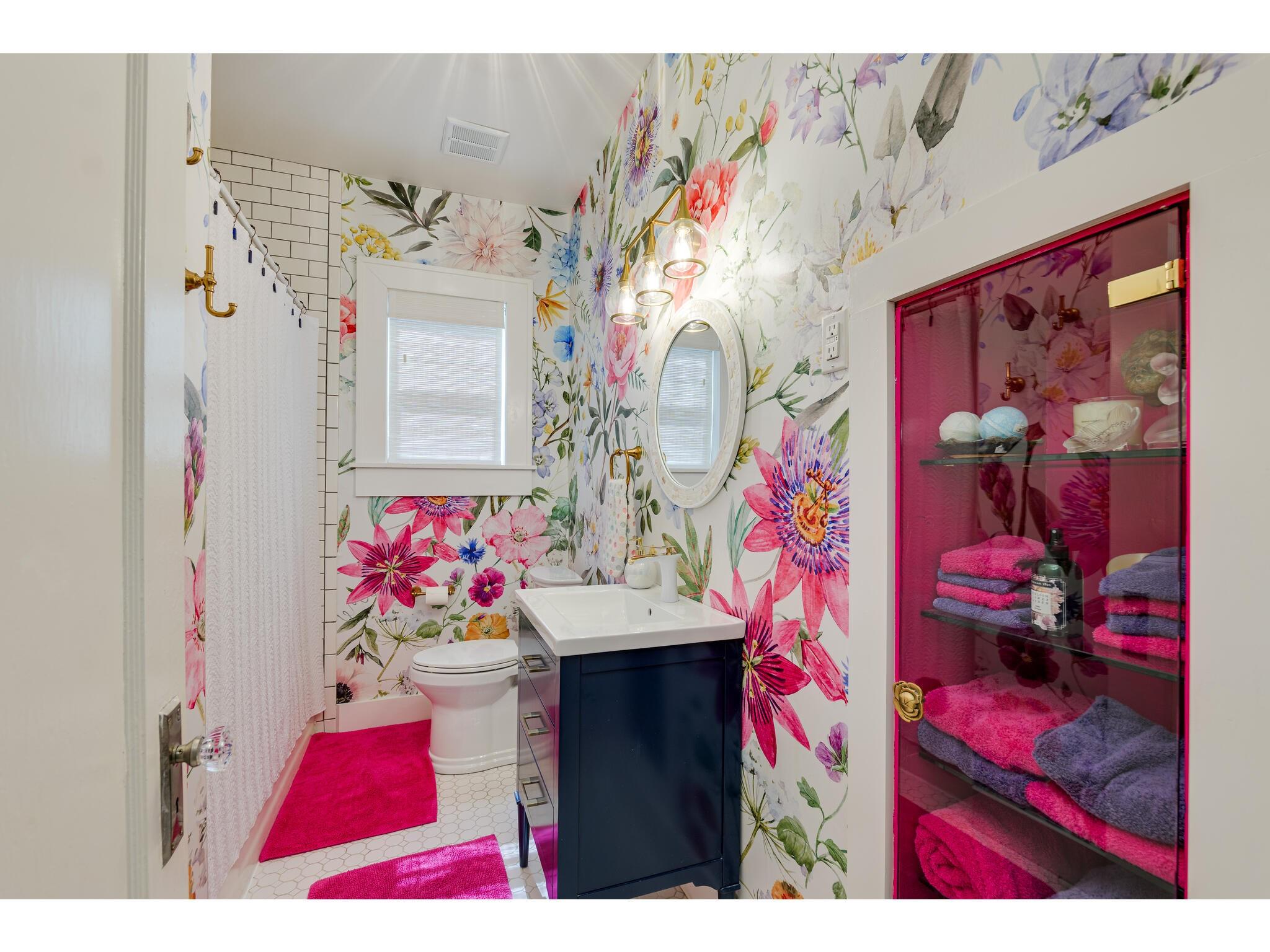 Bathroom with vibrant floral wallpaper, navy vanity, and pink-framed towel cabinet.