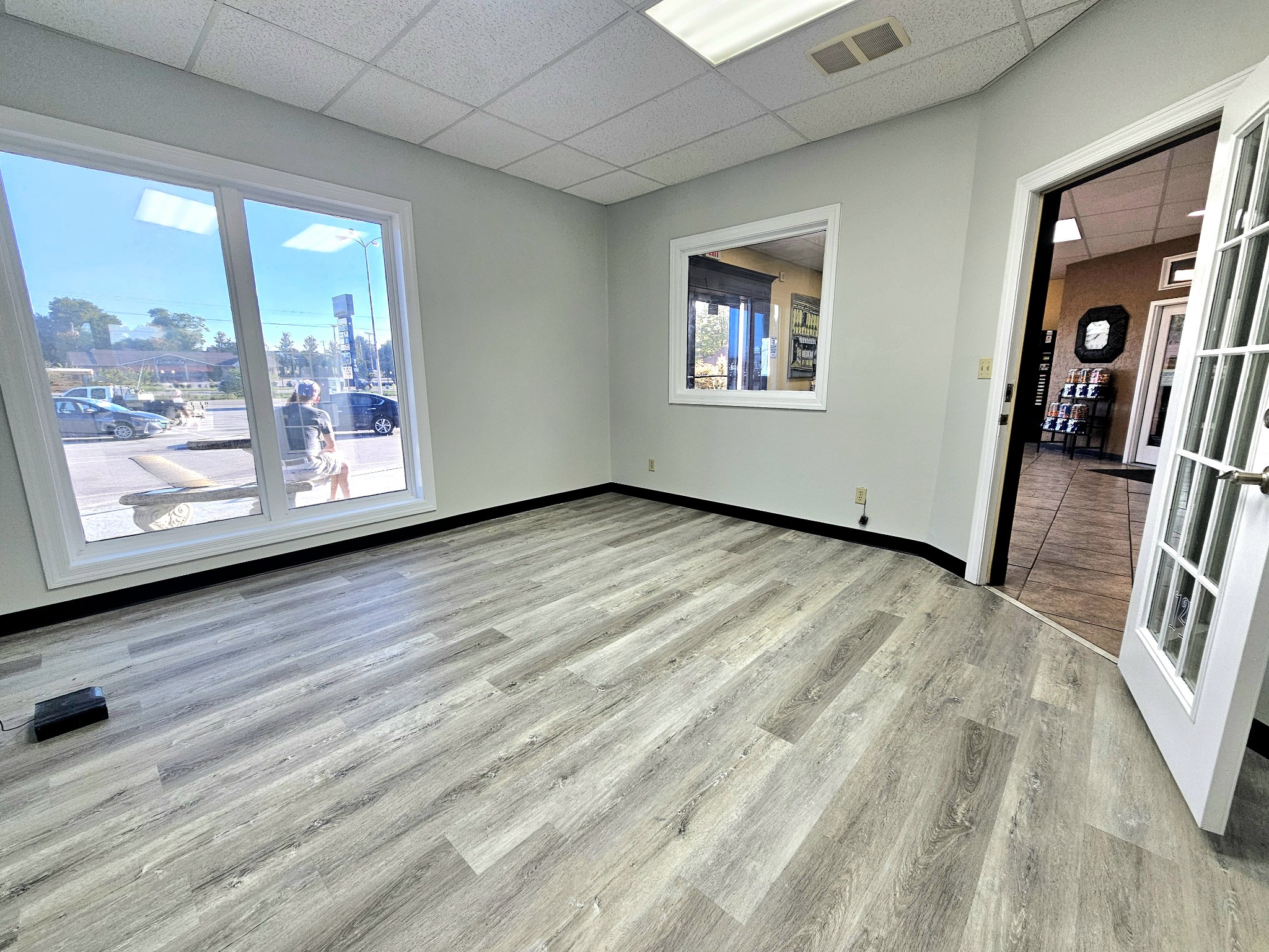 Vacant commercial room with gray wood-look flooring and a large street-facing window.
