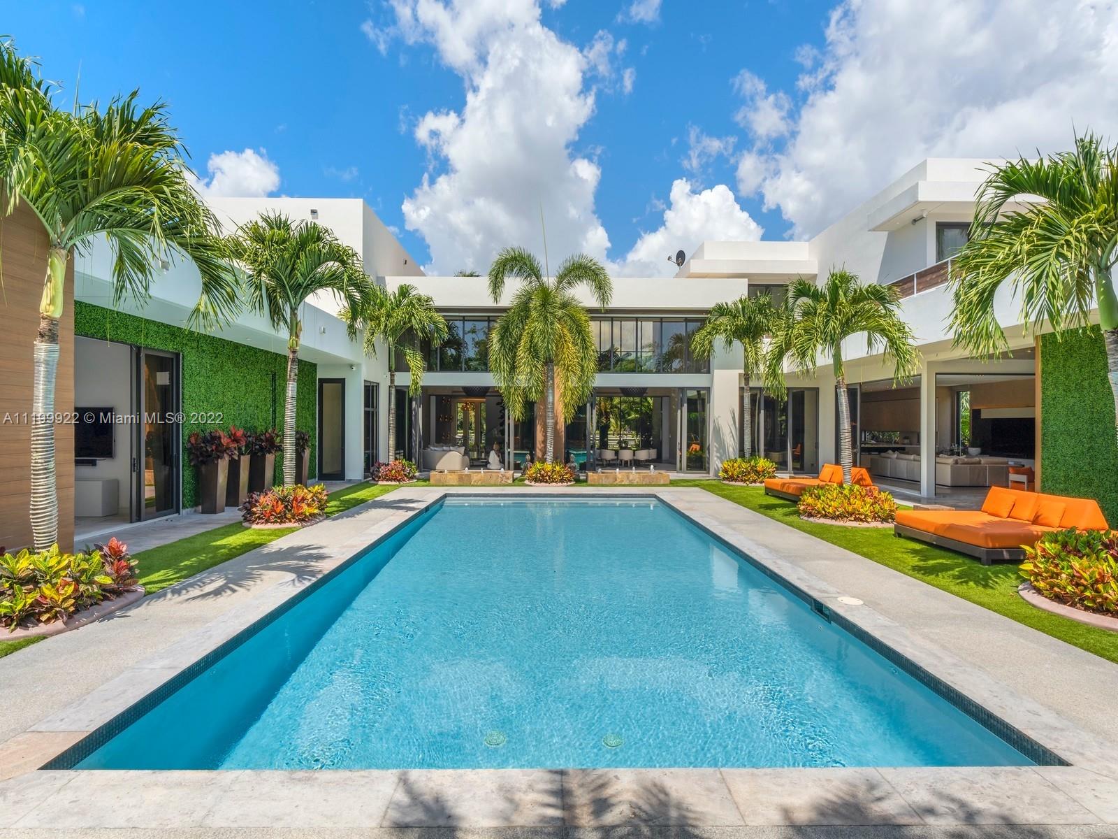 Modern white home with a rectangular pool, palm trees, and orange lounge chairs.