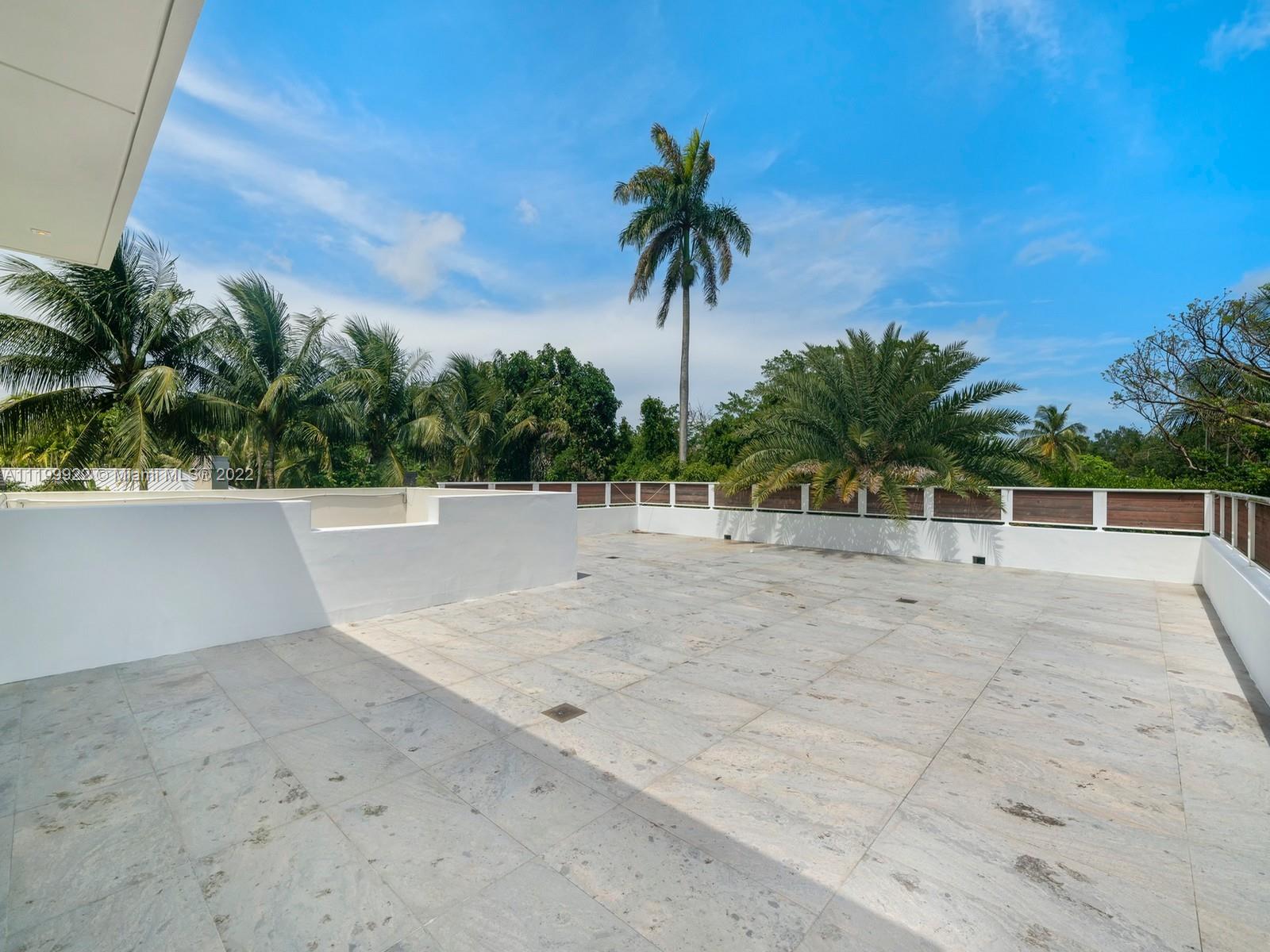 Rooftop terrace with pale stone tiles, wood-panel railings, and views of palm trees.