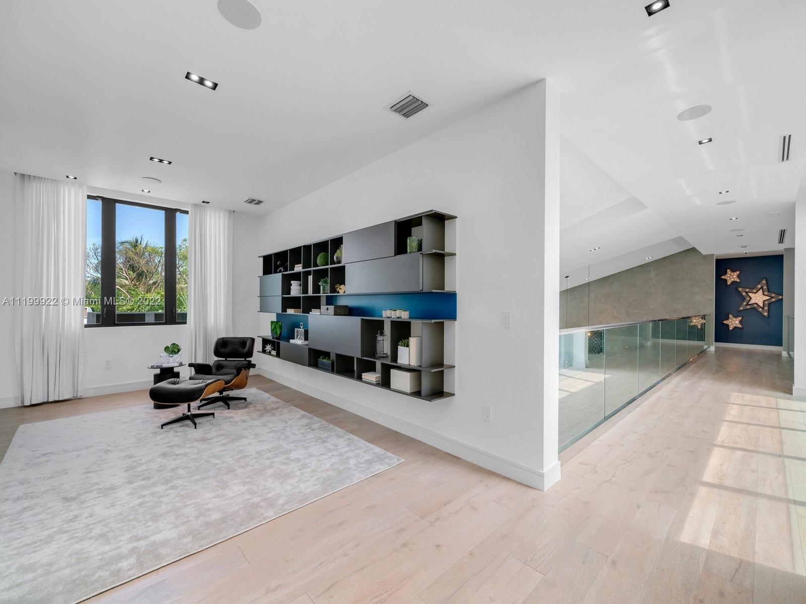 Modern upstairs lounge with a leather chair, built-in shelves, and glass-railed hallway.