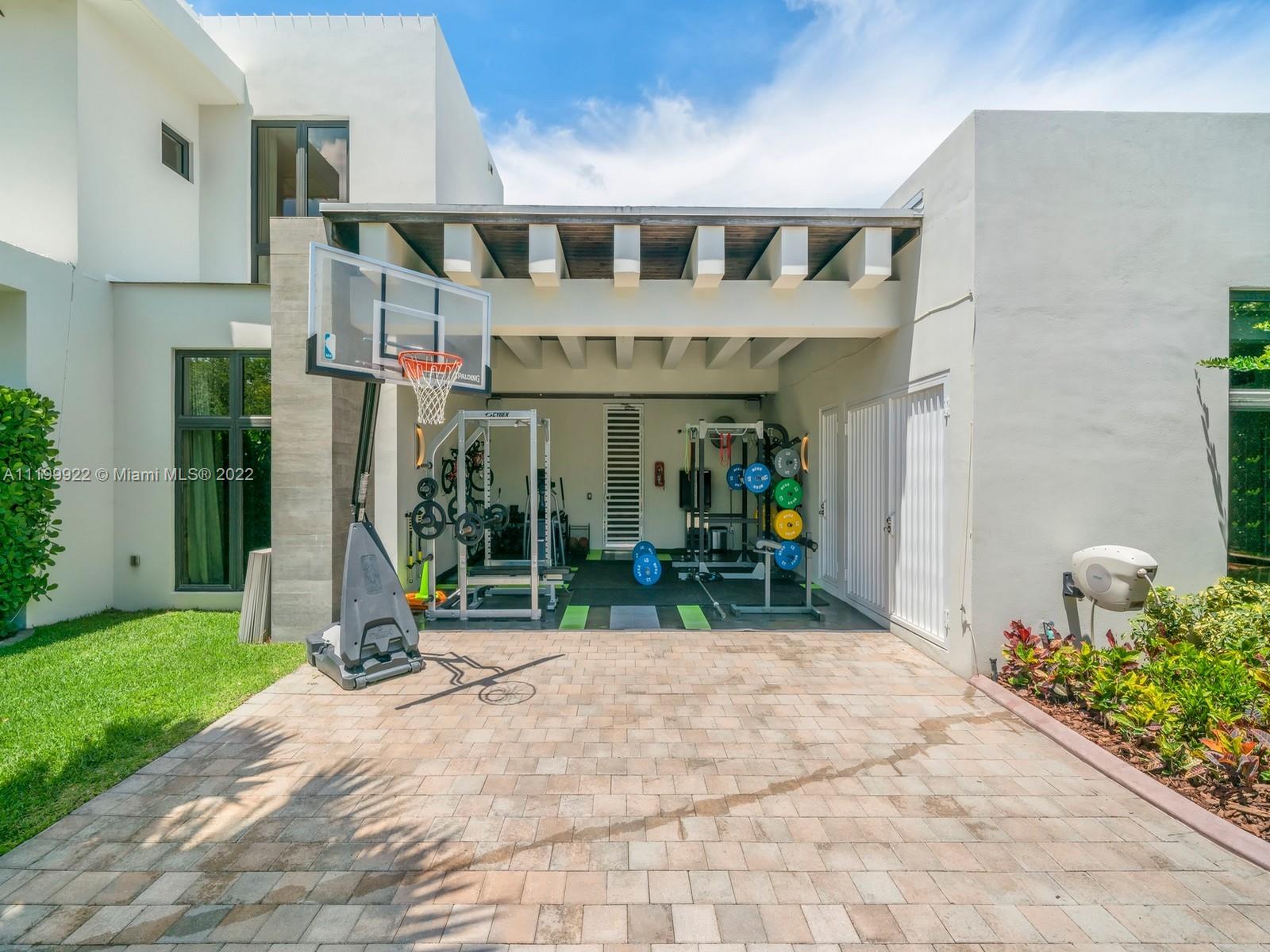 Covered outdoor gym with weight equipment and a basketball hoop in a modern home courtyard.