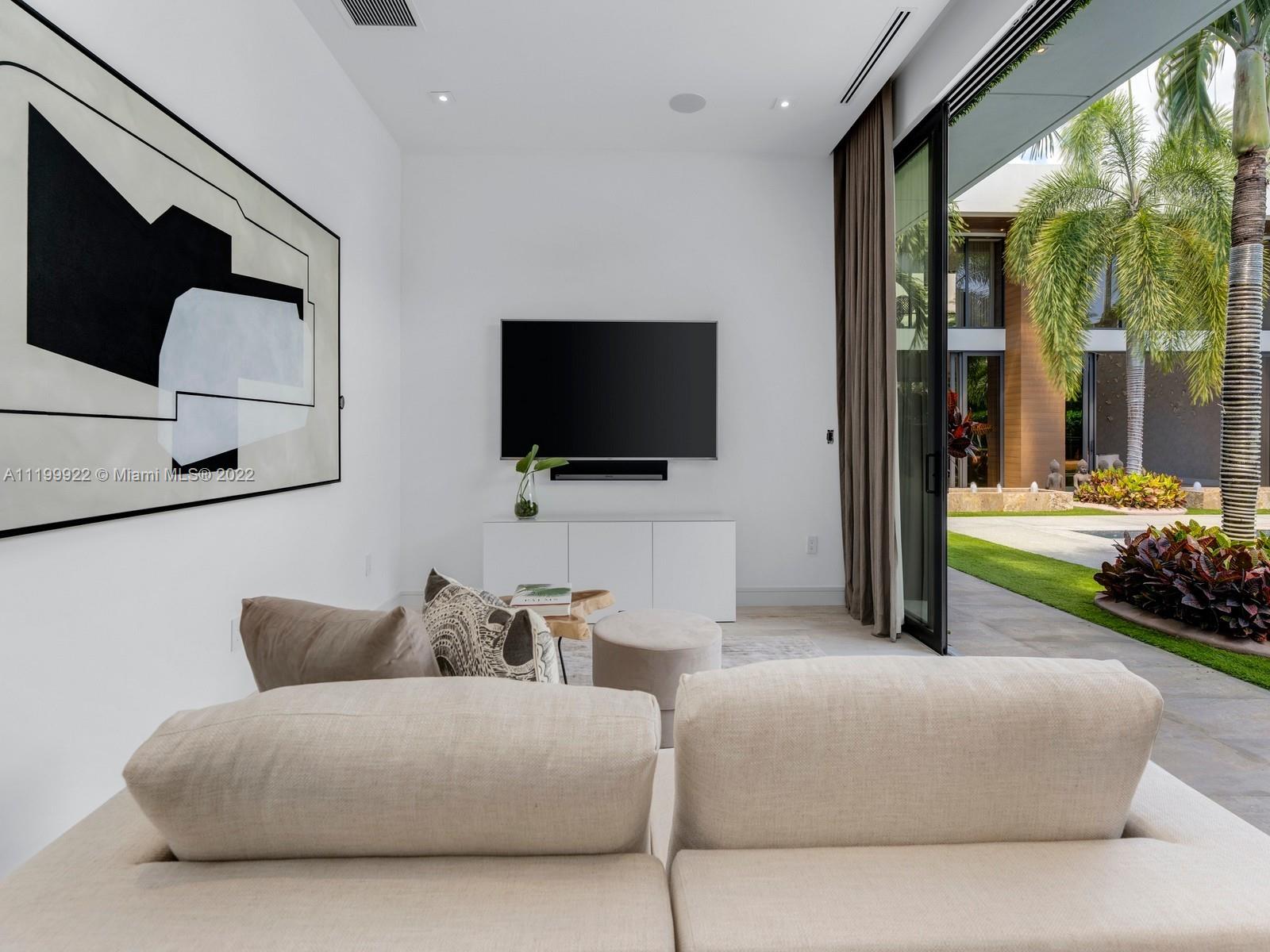 Modern living room with abstract wall art and sliding glass doors to a palm-lined courtyard.
