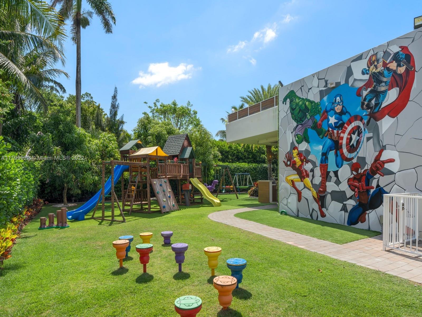 Outdoor playground with a wooden play structure, colorful stools, and a superhero mural on the wall.