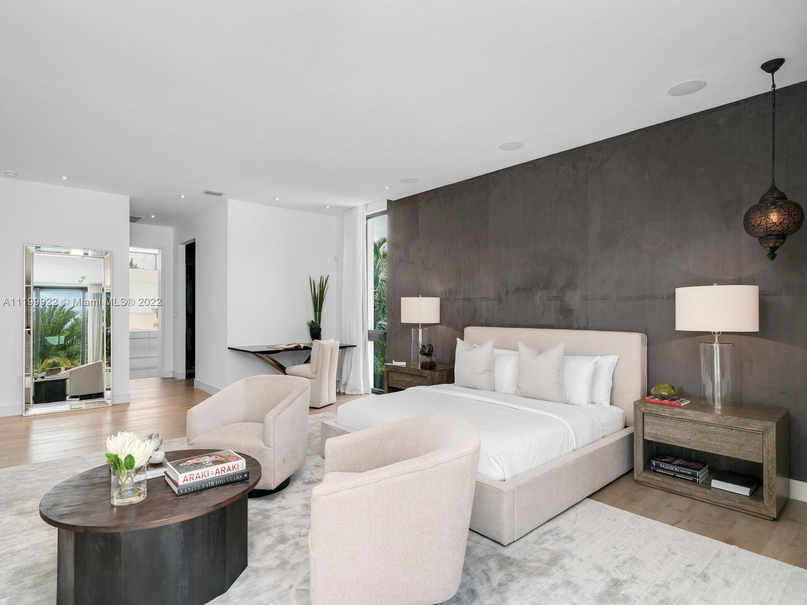 Modern bedroom with a white upholstered bed against a dark textured wall and pale lounge chairs.