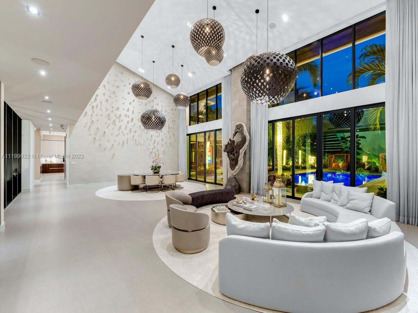Double-height living room with curved white sofas, globe pendant lights, and glass doors overlooking a pool.