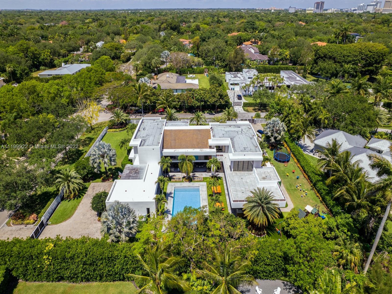 Aerial view of modern white home with swimming pool amid lush greenery.