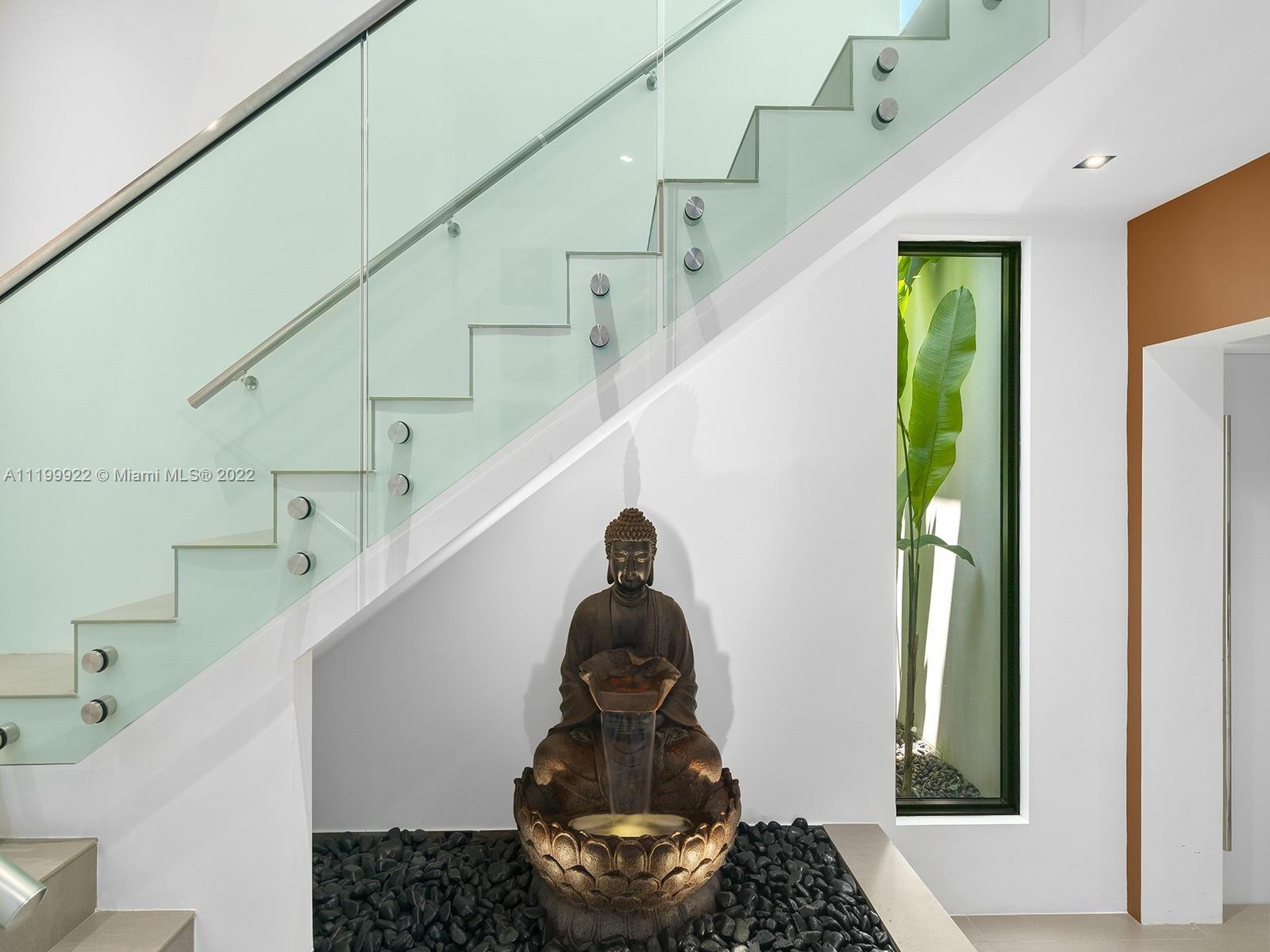 Modern foyer with a glass-railed staircase and Buddha fountain surrounded by black stones.