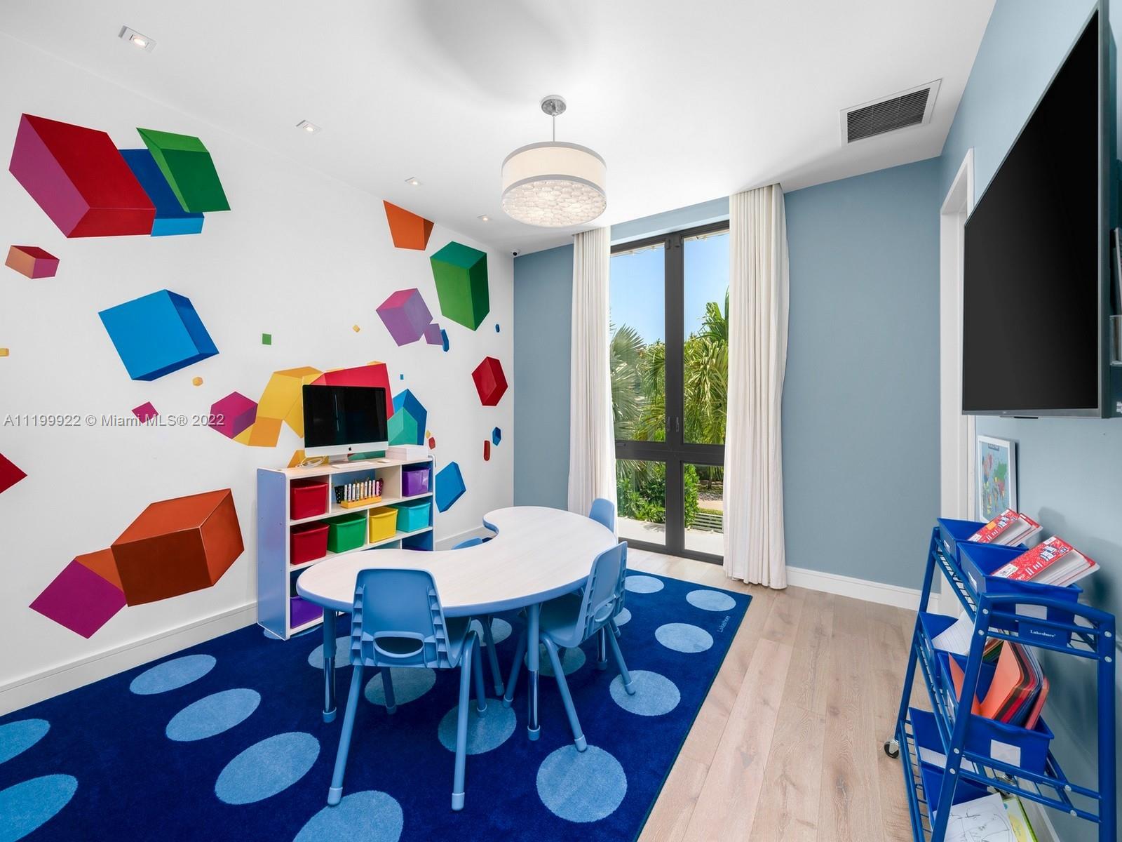 Playroom with colorful geometric wall art, blue furniture, dotted rug, and glass doors overlooking greenery.
