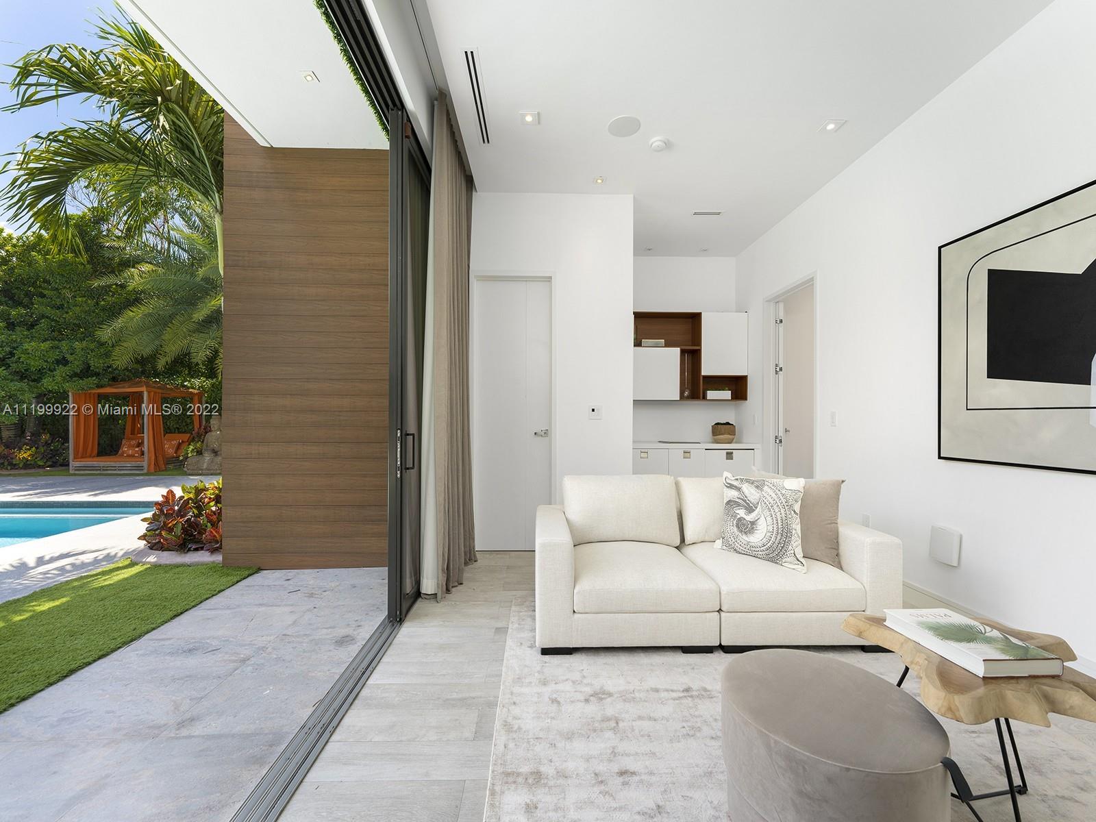 Living room with a white sofa and sliding doors opening to a palm-lined poolside garden.