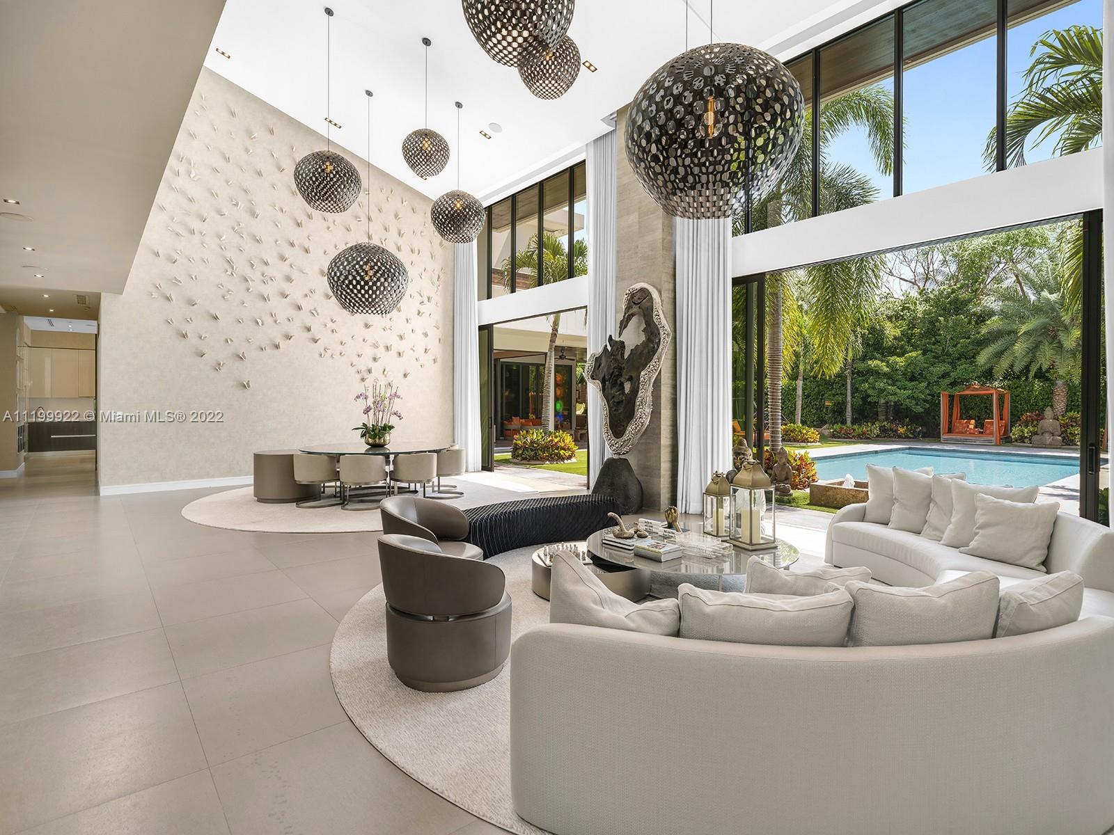 Double-height living room with sculptural pendant lights and floor-to-ceiling windows overlooking the pool.