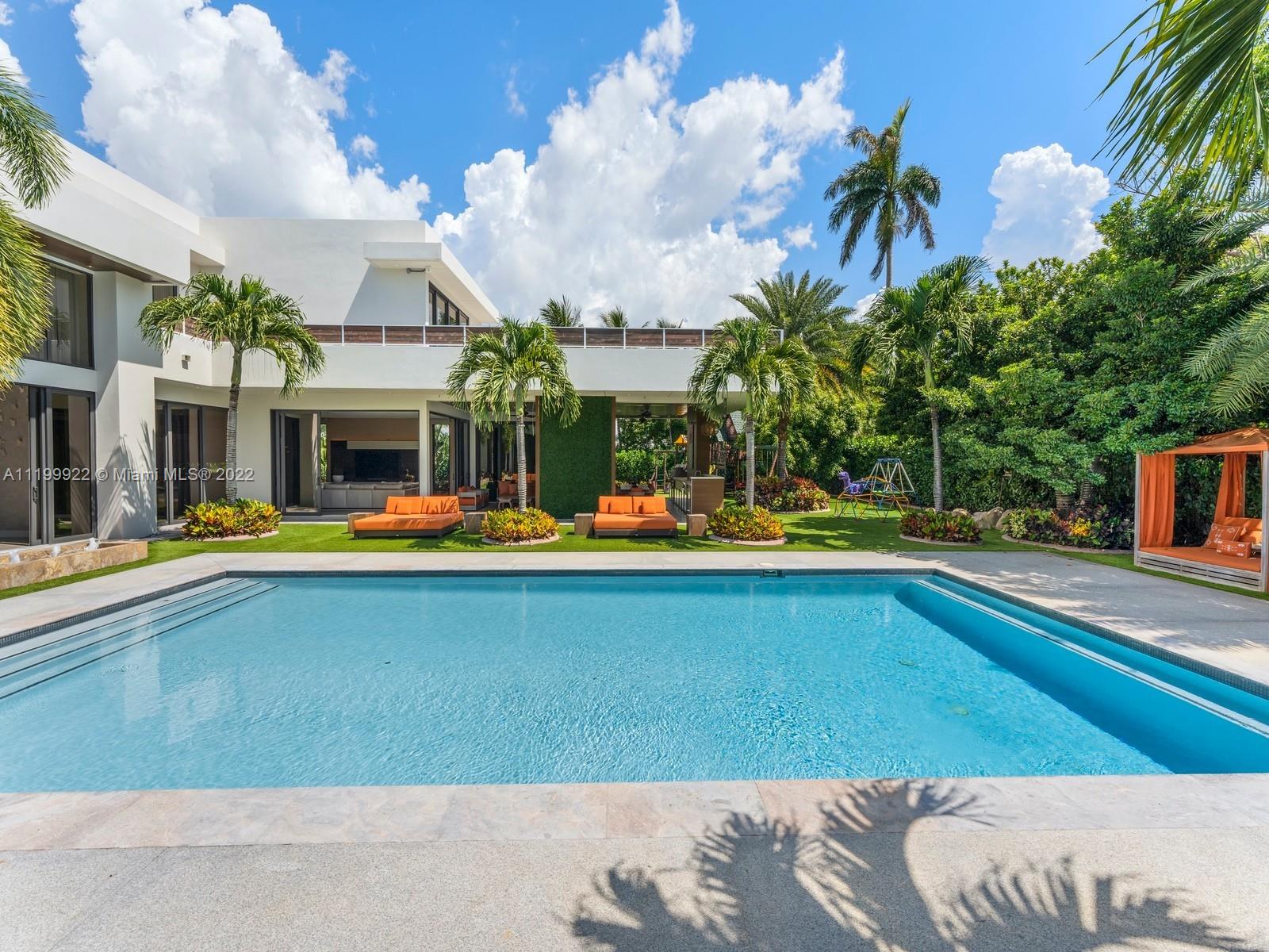 Modern white home with a broad blue swimming pool, palms, and furnished patio.