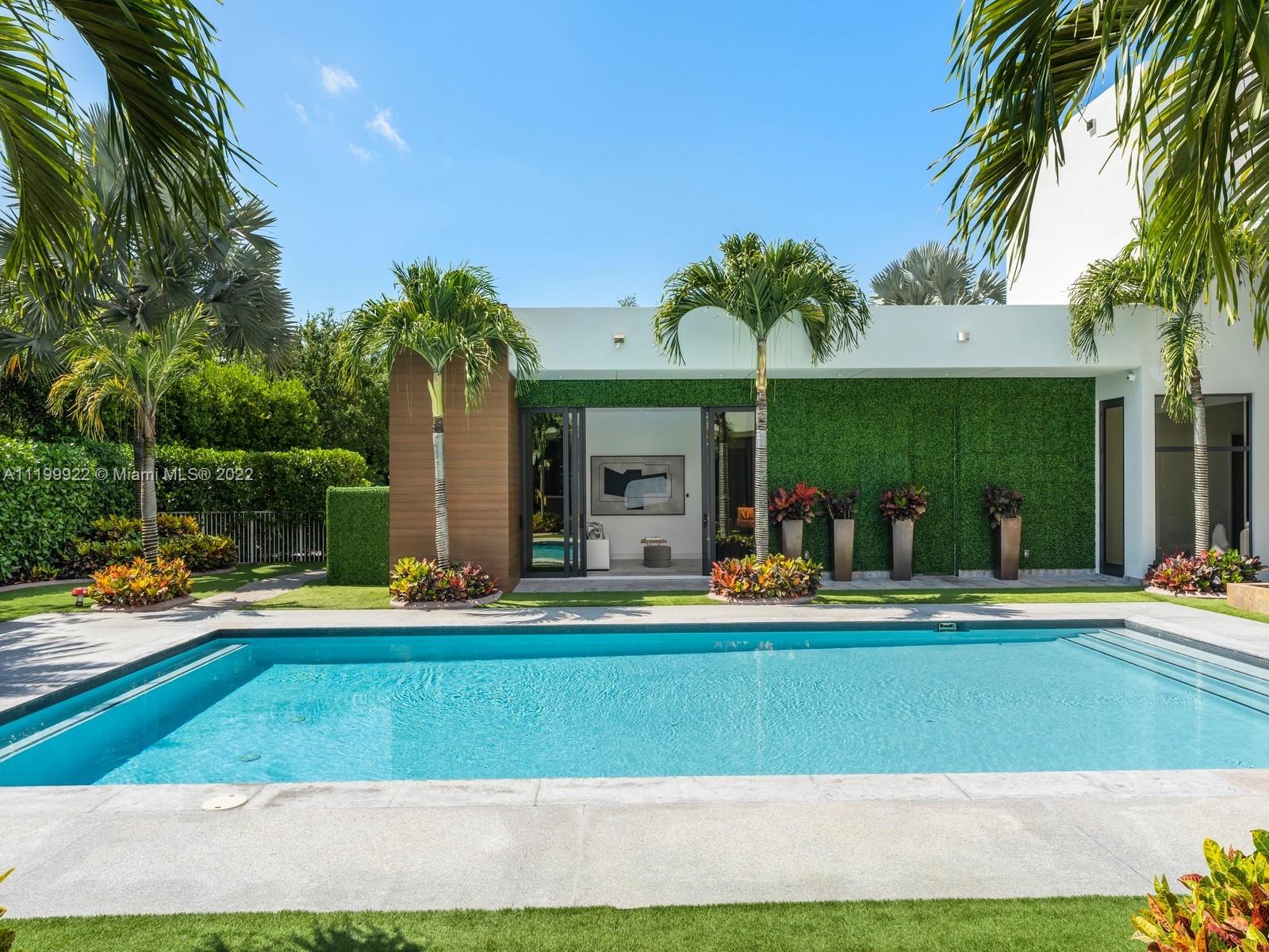 Modern home behind a turquoise pool, with a green living wall and tropical palms.
