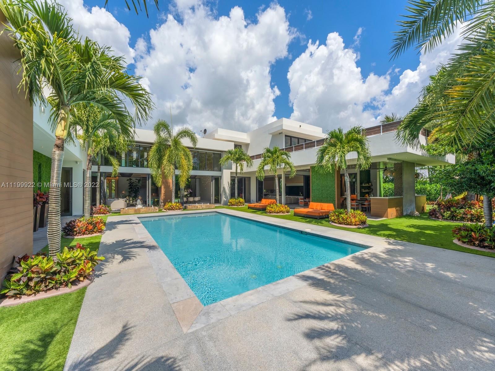 Modern two-story home behind a swimming pool, framed by palms and orange lounge chairs.