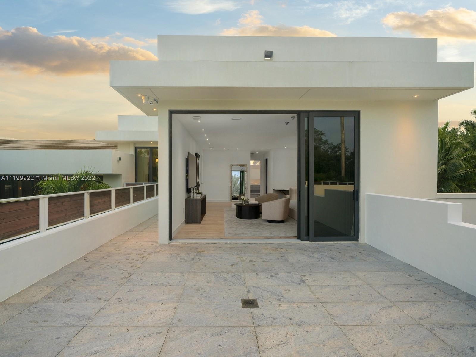 Stone terrace outside a modern home, with wide sliding doors opening to a furnished living room.