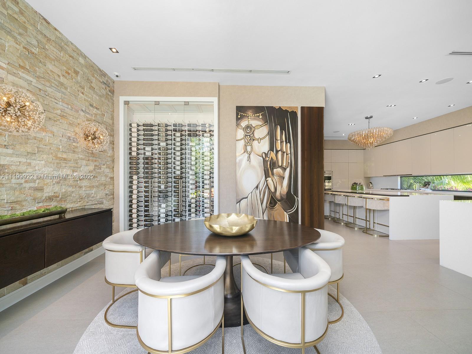 Dining area with a round table, white chairs, glass-front wine display, and adjoining modern kitchen.
