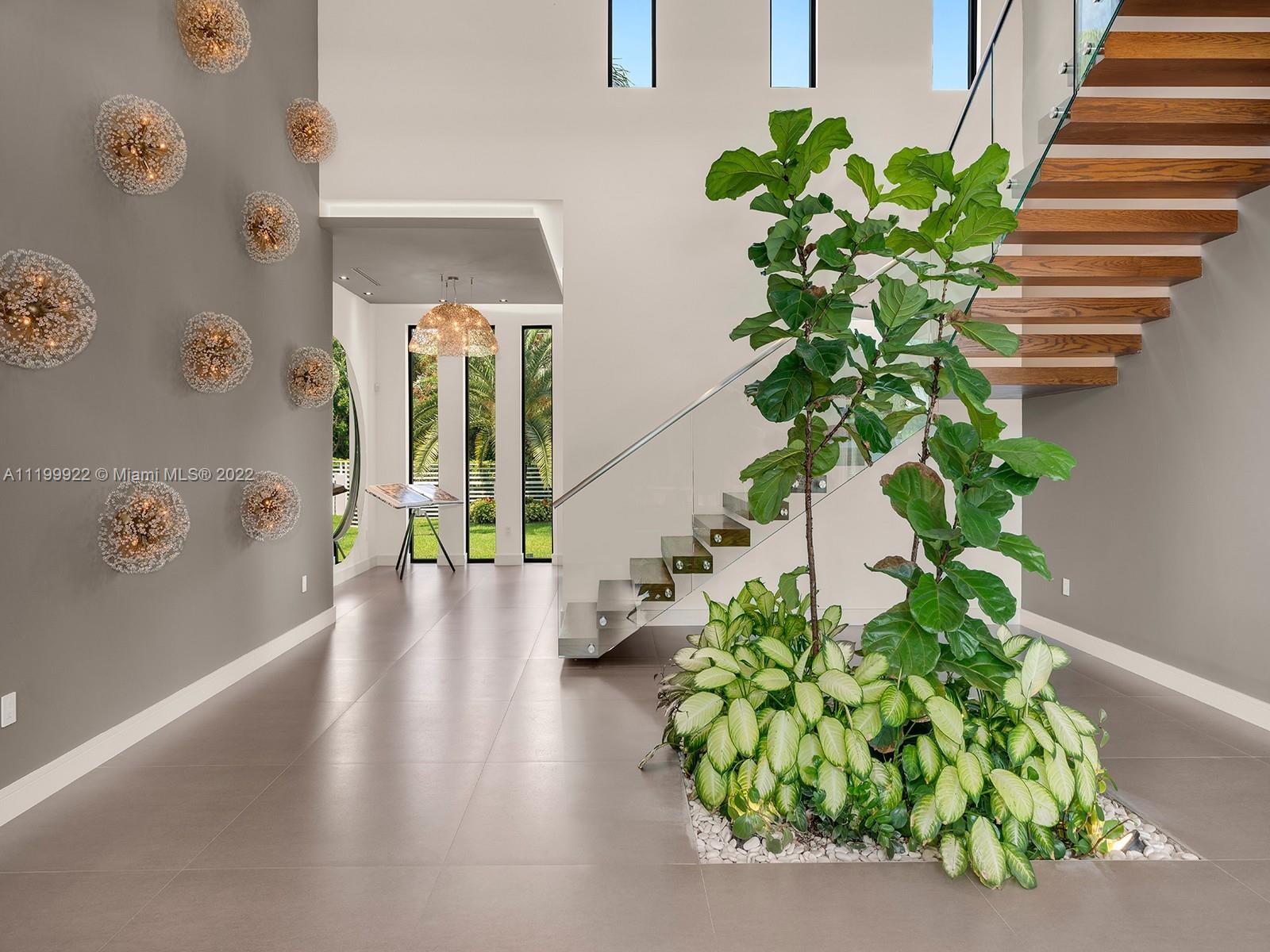 Modern foyer with a floating wood staircase, tall windows, and a leafy indoor garden.