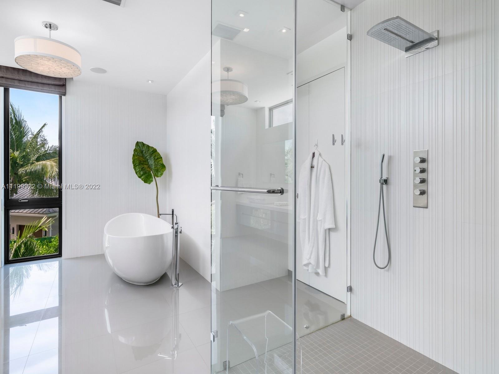 Bright bathroom with a freestanding tub, glass shower, rain showerhead, and tall window overlooking greenery.