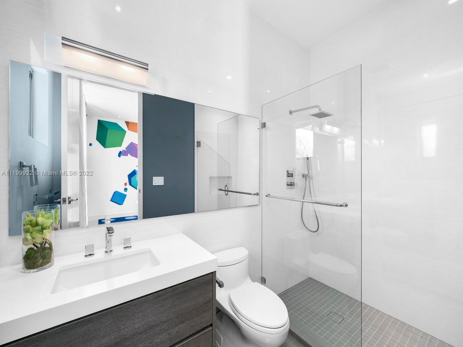 Modern white bathroom with dark wood vanity, glass shower, and a mirror reflecting colorful geometric wall art.