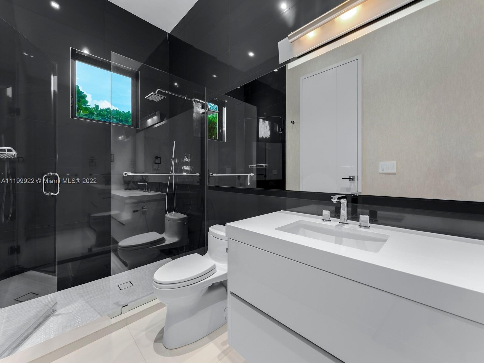 Modern bathroom with glossy black-tile shower, rainfall showerhead, white toilet, and broad white vanity.