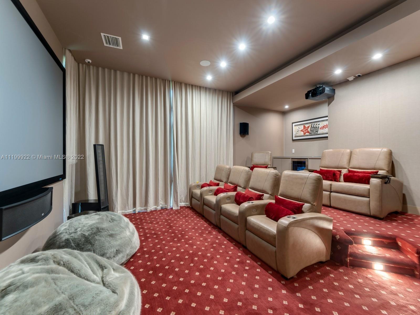 Home theater with beige reclining seats, a large screen, ceiling-mounted projector, and red patterned carpet.
