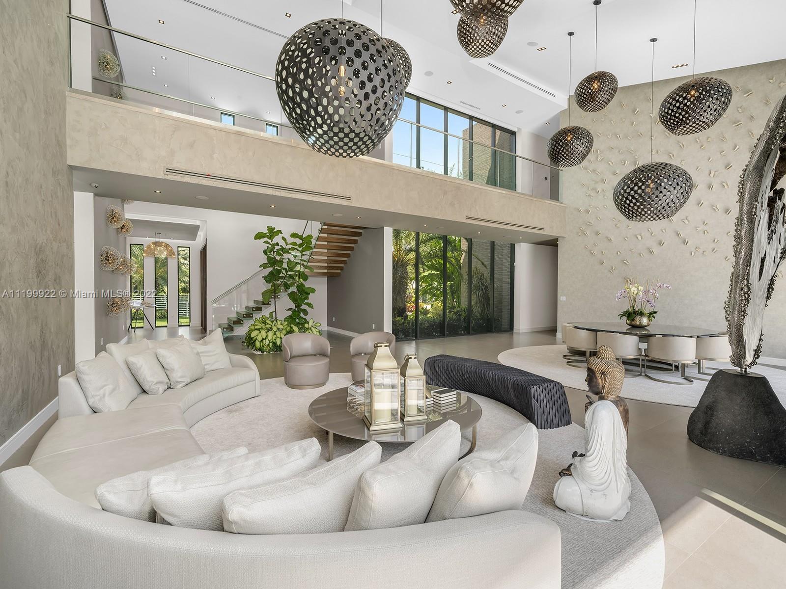 Double-height living room with a curved white sectional, floating staircase, and dramatic pendant lights.