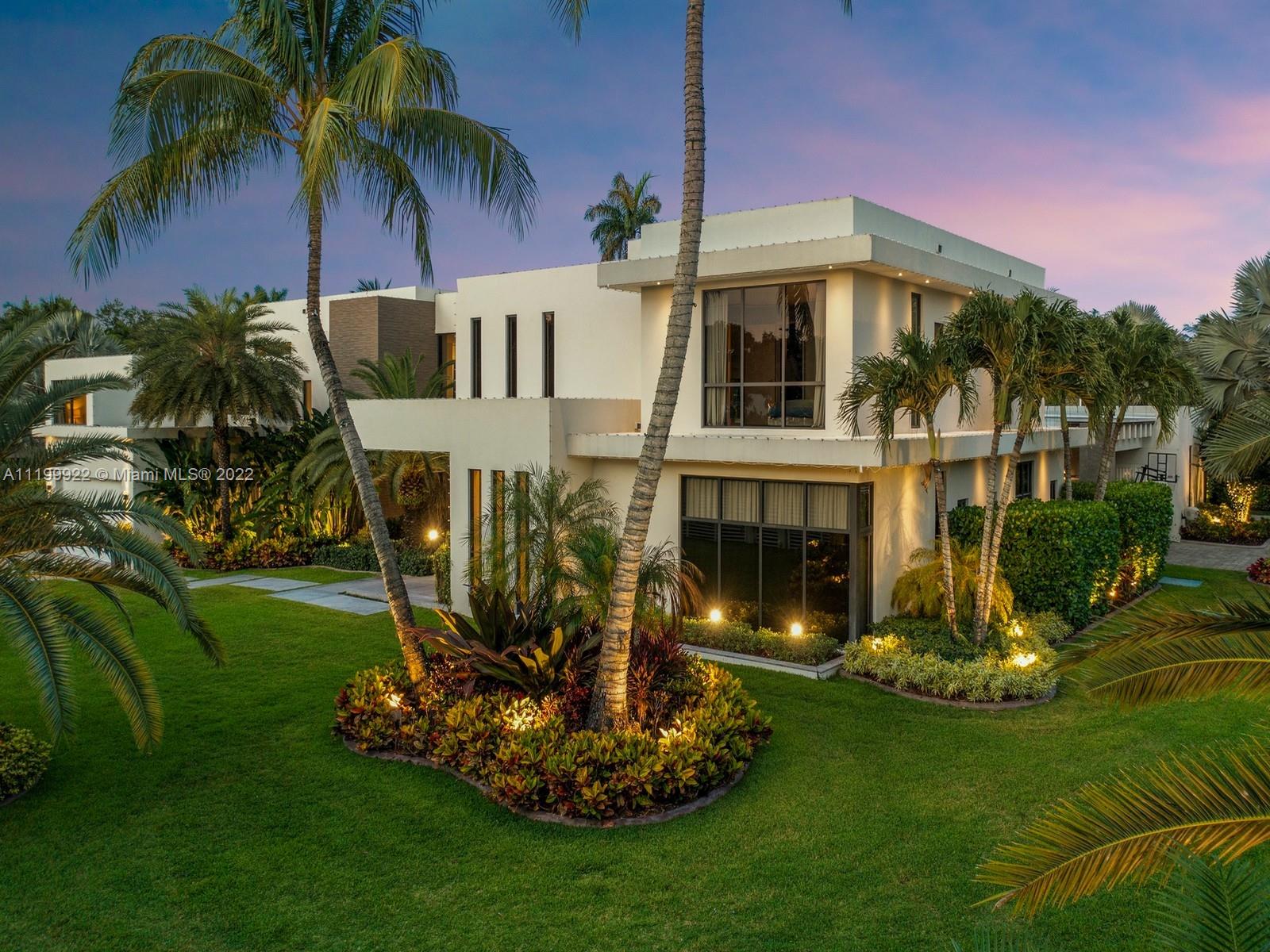 Modern two-story white house framed by palm trees and tropical landscaping at dusk.