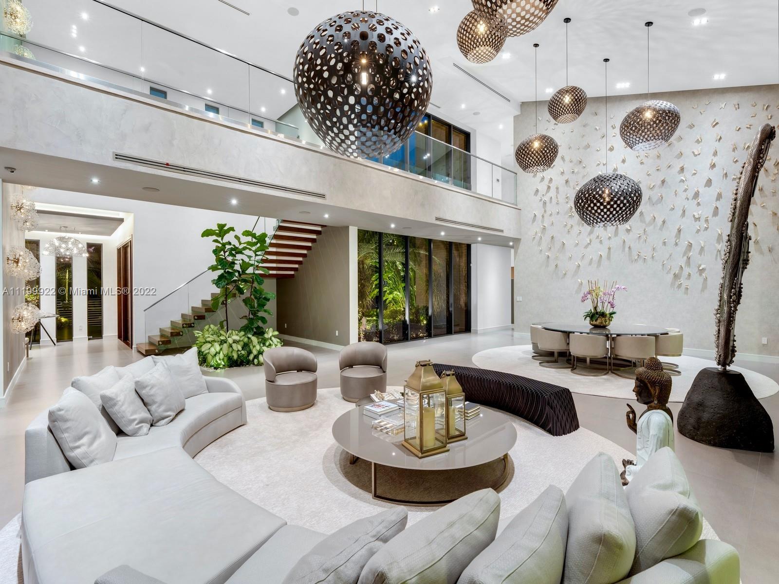 Double-height modern living room with a white sectional, sculptural pendant lights, and a glass-railed upper gallery.