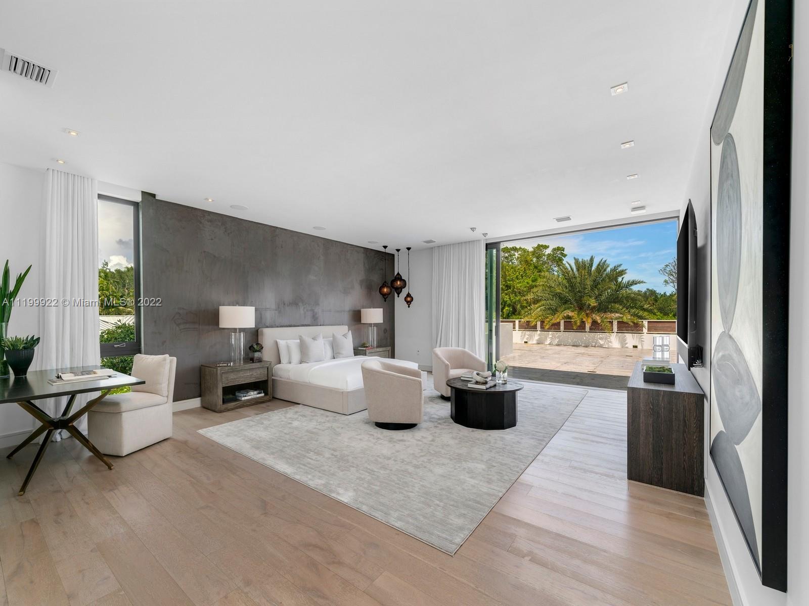 Modern bedroom with a concrete accent wall and sliding doors opening onto a tropical terrace.