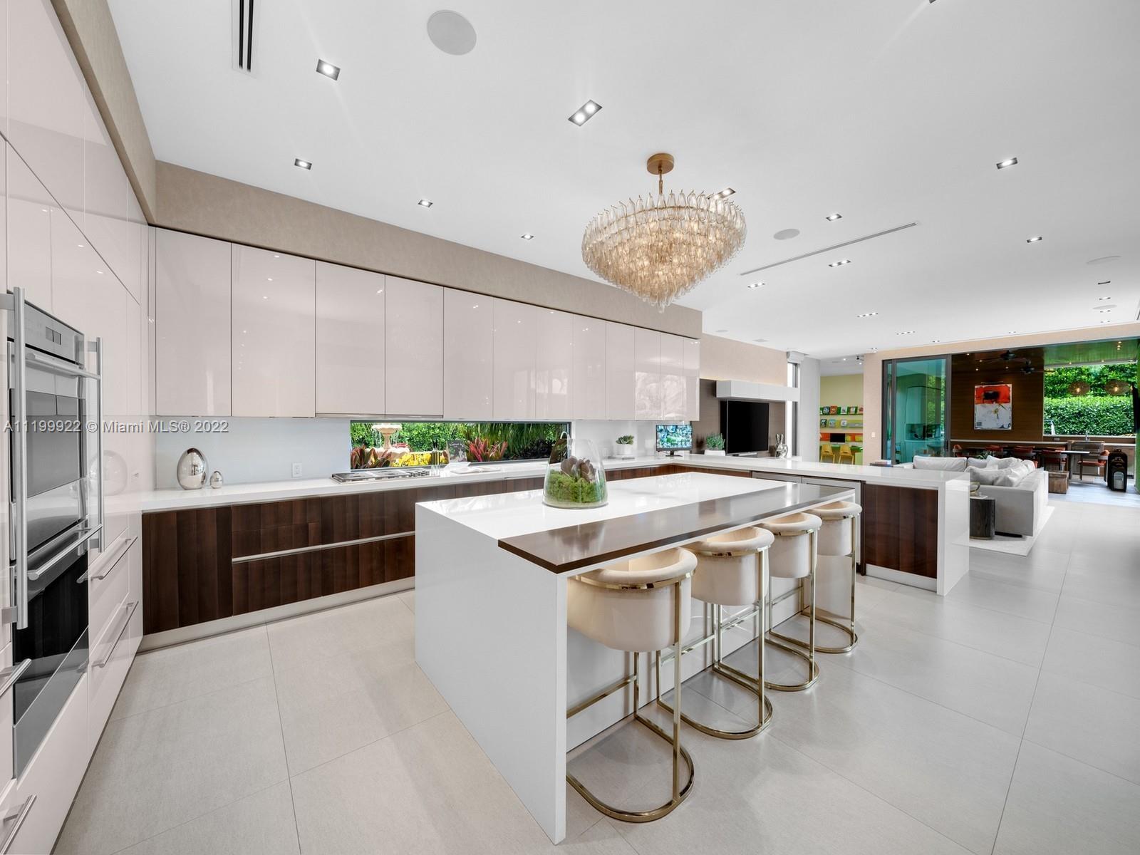 Modern kitchen with a large island, four stools, glossy white cabinets, and a sculptural chandelier.