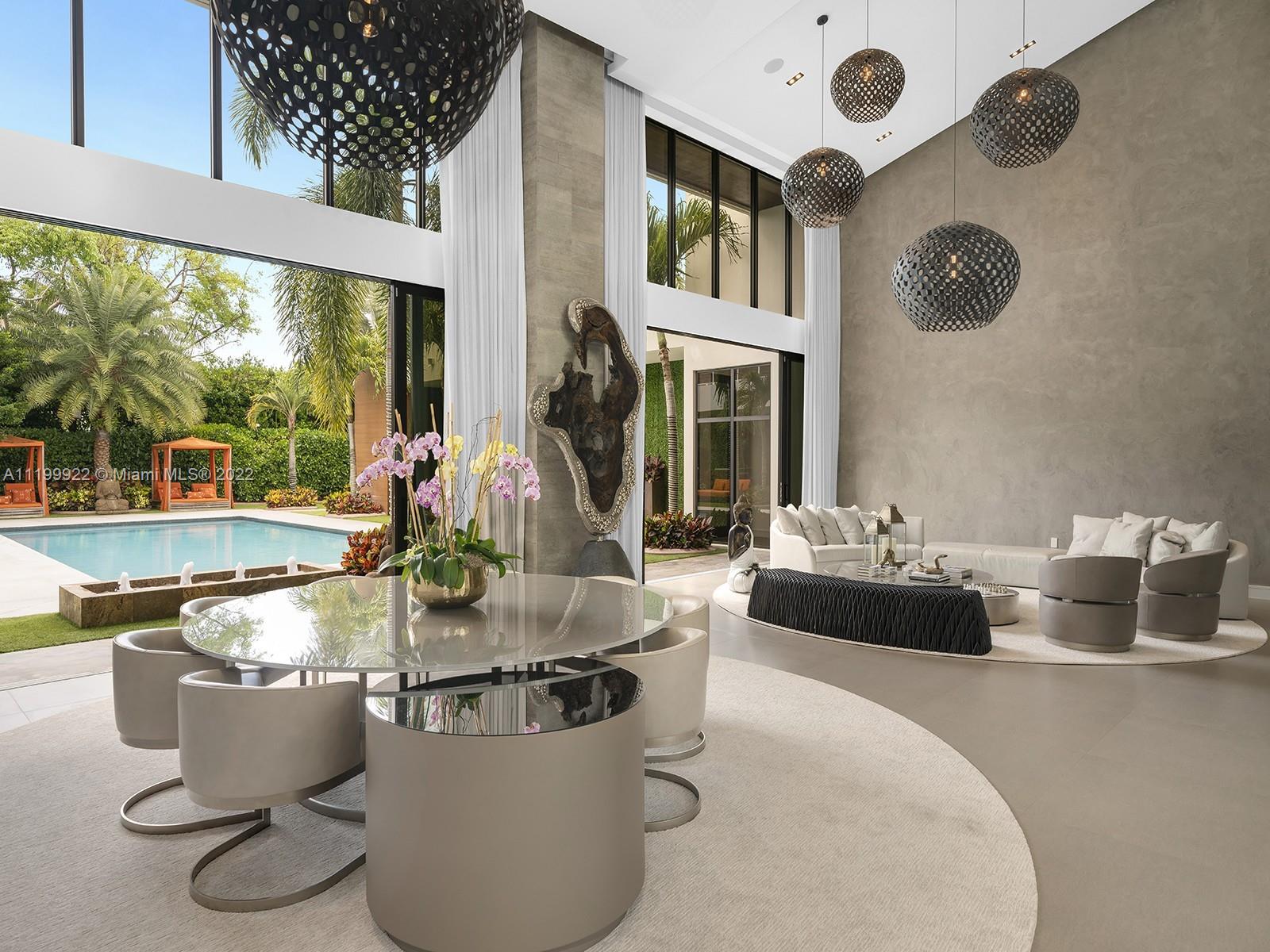 Double-height living and dining room with sculptural pendant lights and views of a backyard pool.