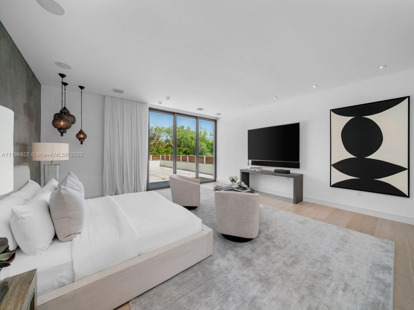 Modern bedroom with a white bed, sculptural pendant lights, and sliding doors to a tree-lined terrace.