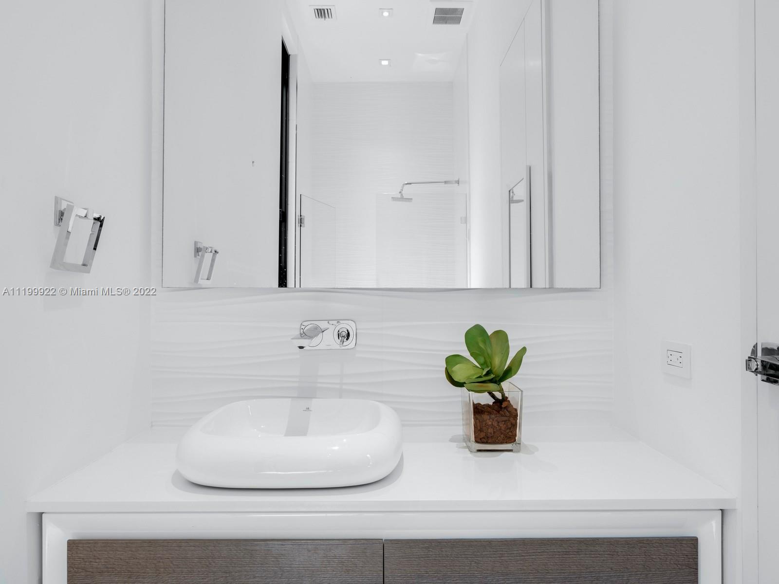 Modern white bathroom vanity with a vessel sink, chrome faucet, and potted plant.