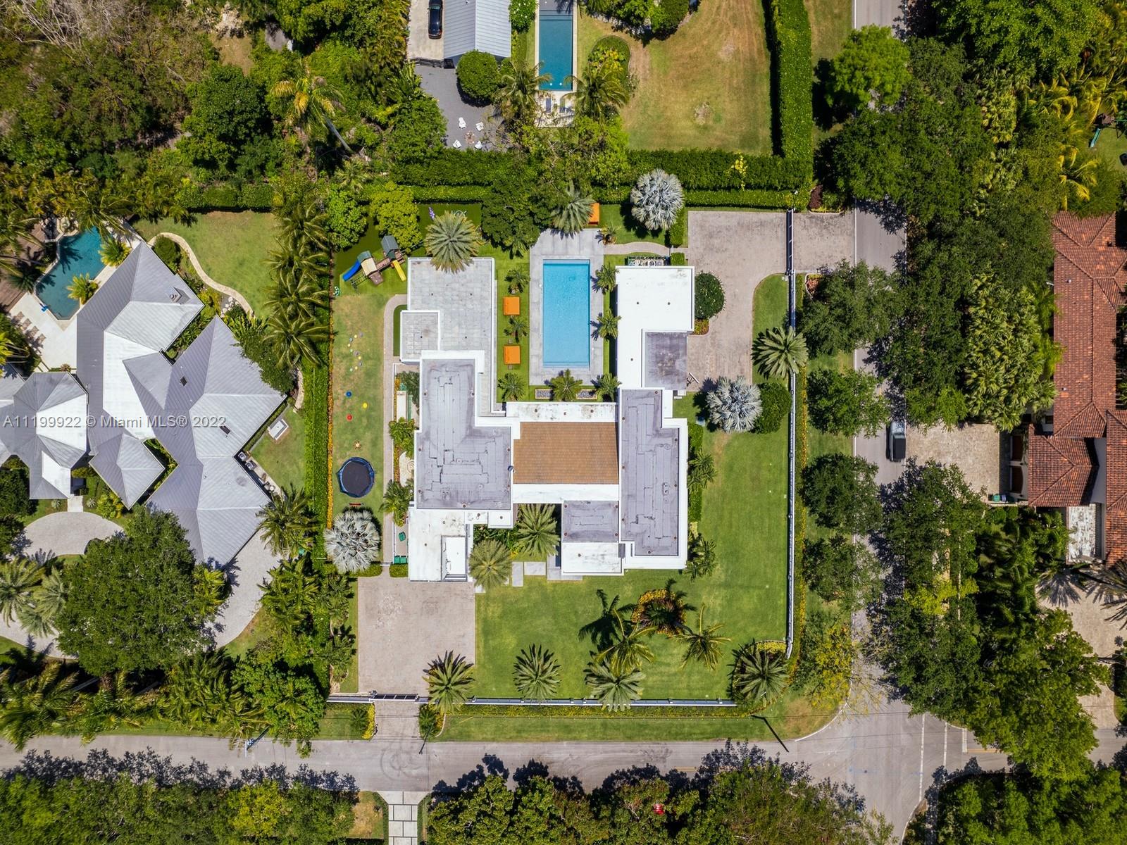 Aerial view of a modern home with a rectangular pool, palm-lined lawn, and driveway.
