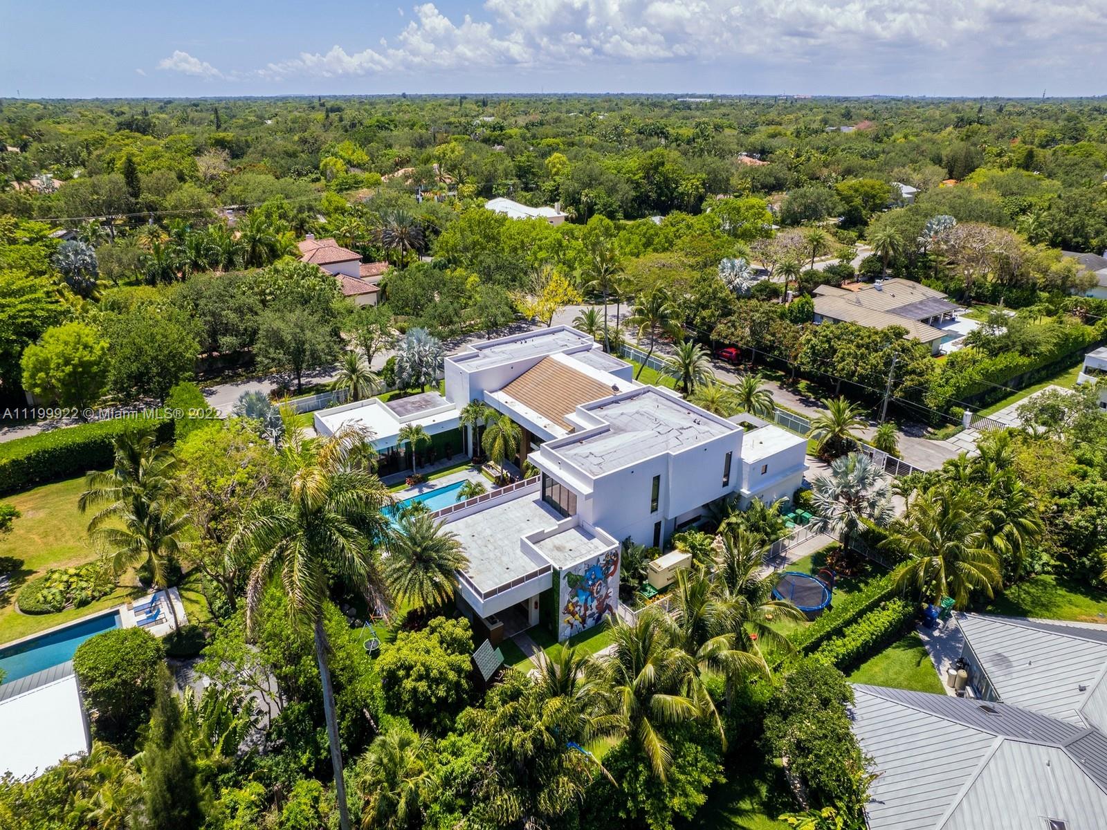 Aerial view of a modern home with a pool, rooftop terraces, and tropical landscaping.